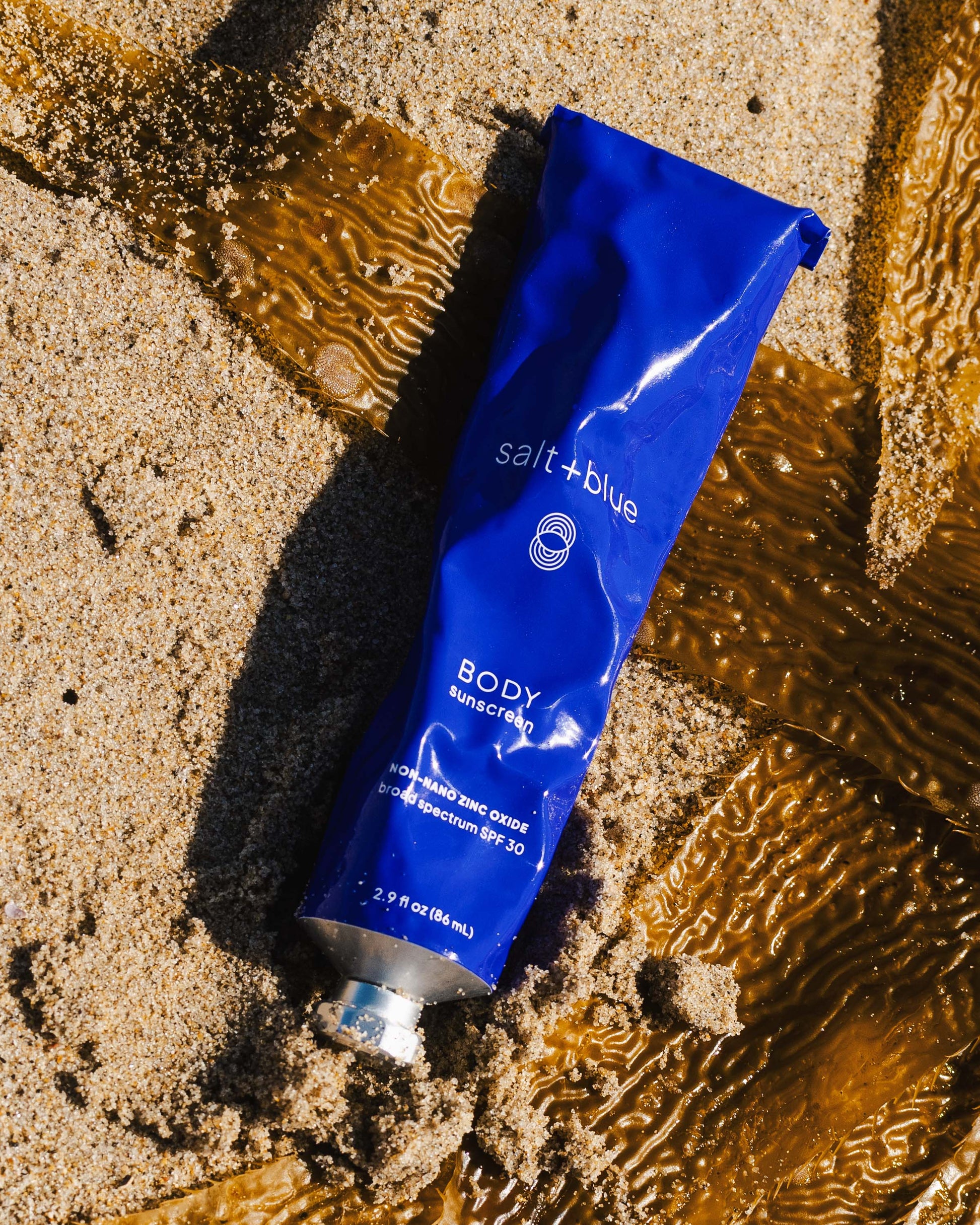 Blue tube of salt+blue body sunscreen on wet sand