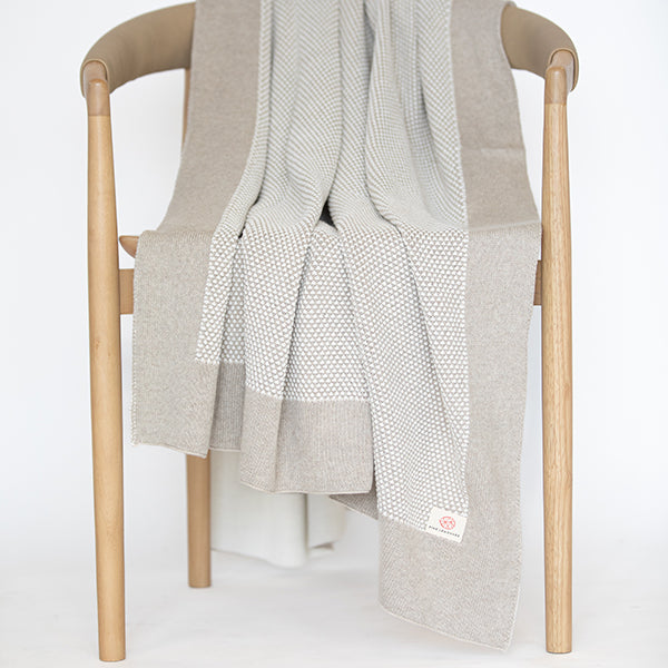 Beige and white textured cotton throw draped over a wooden chair on a white background.