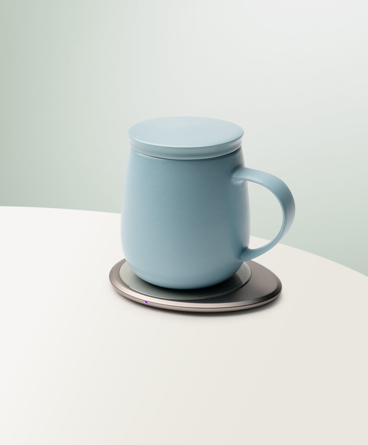 Ui 3 Self-Heating Ceramic Mug 12 fl oz / 355 mL in Moonmist Blue with lid angled top-side view on OHOM Charging Pad 3