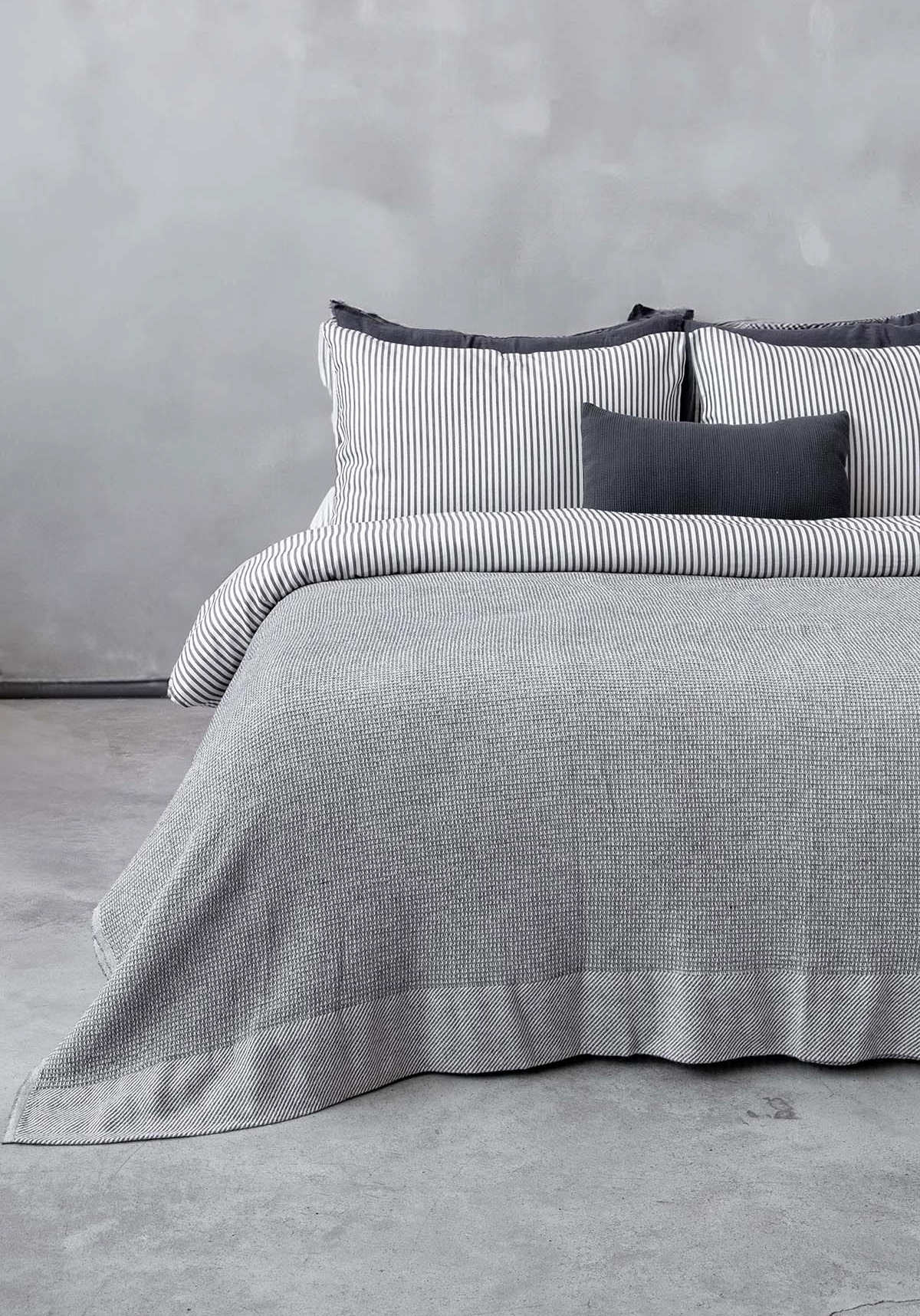 Gray textured bedspread with striped pillows on a gray background