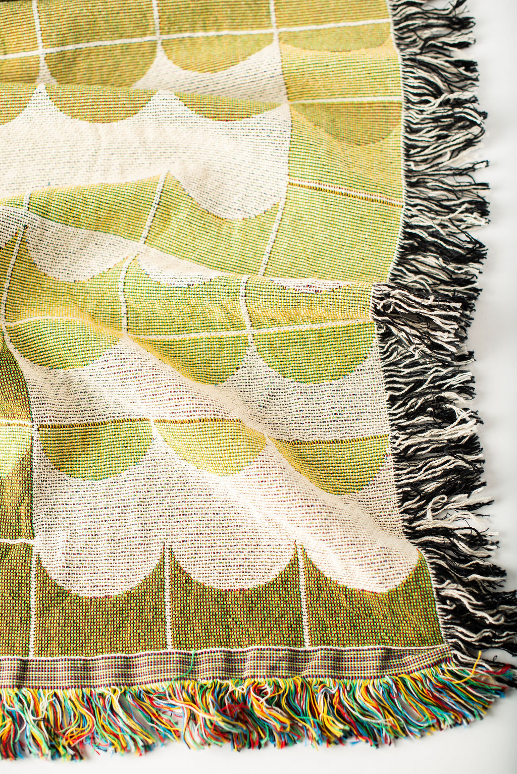Close-up of Quinn Meadow green, gold, and cream geometric scallop jacquard woven blanket with fringe