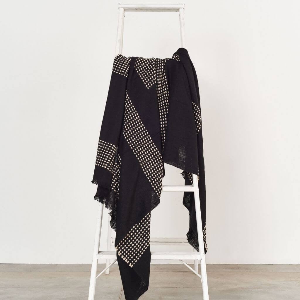 Walnut Black Yak With Hand Knotted Merino Stripes Handloom Throw draped on a white ladder, showcasing its unique design.