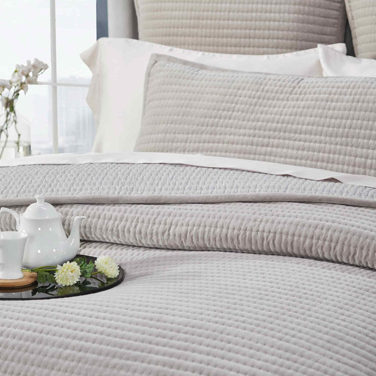 CL-188-9496_6|Detail view of a soft grey quilted coverlet on a bed, highlighting its subtle channel texture and comfort.