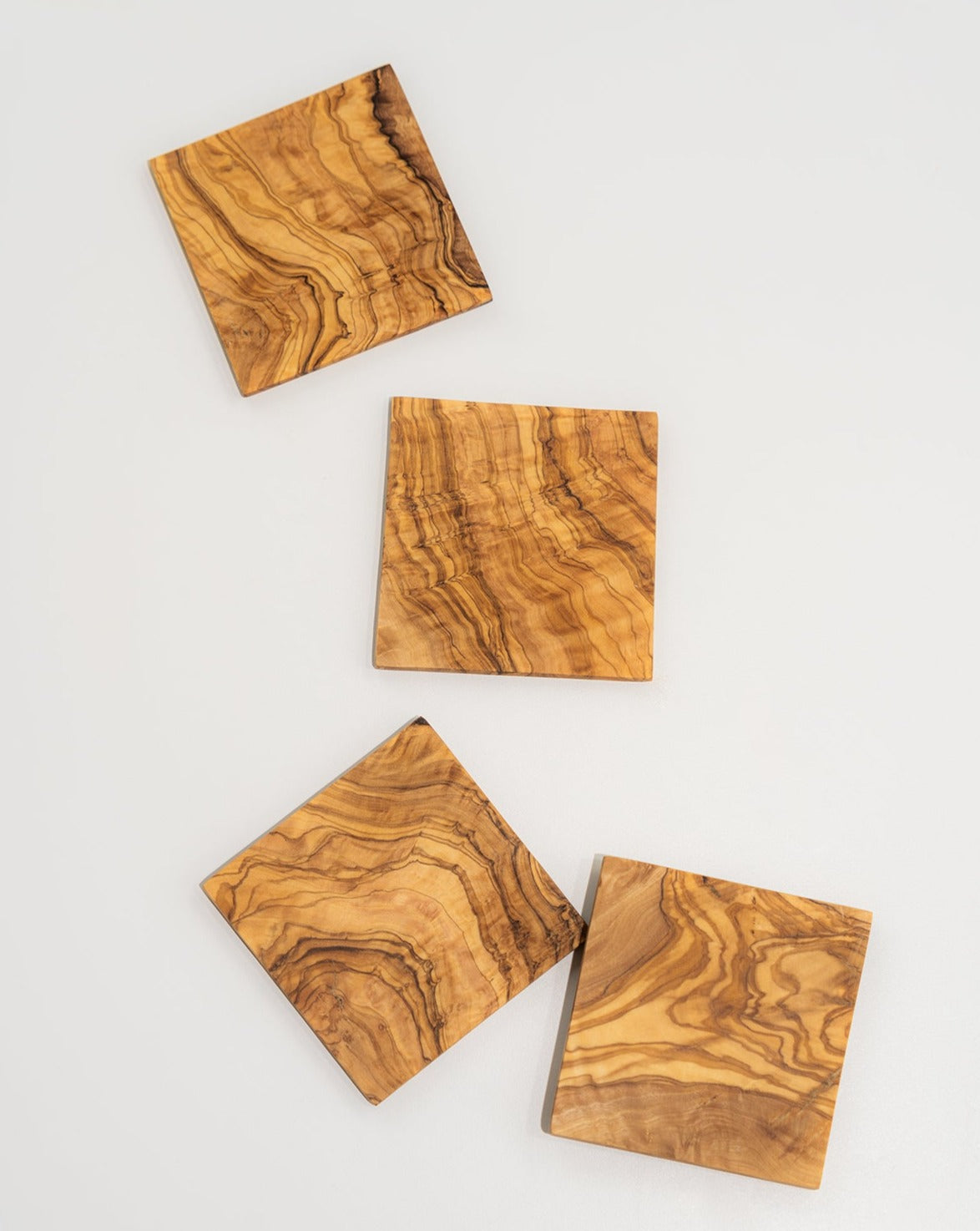 A set of four square coasters made of natural olivewood, displayed on a white background.