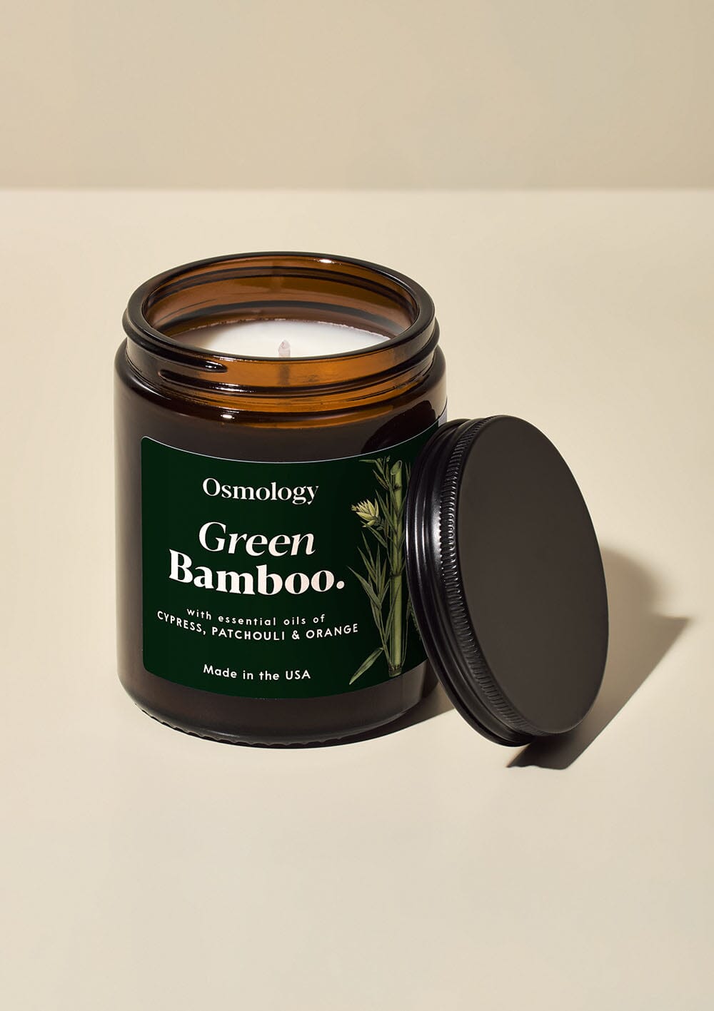 Osmology Green Bamboo jar candle, with lid leaning against it, on white background