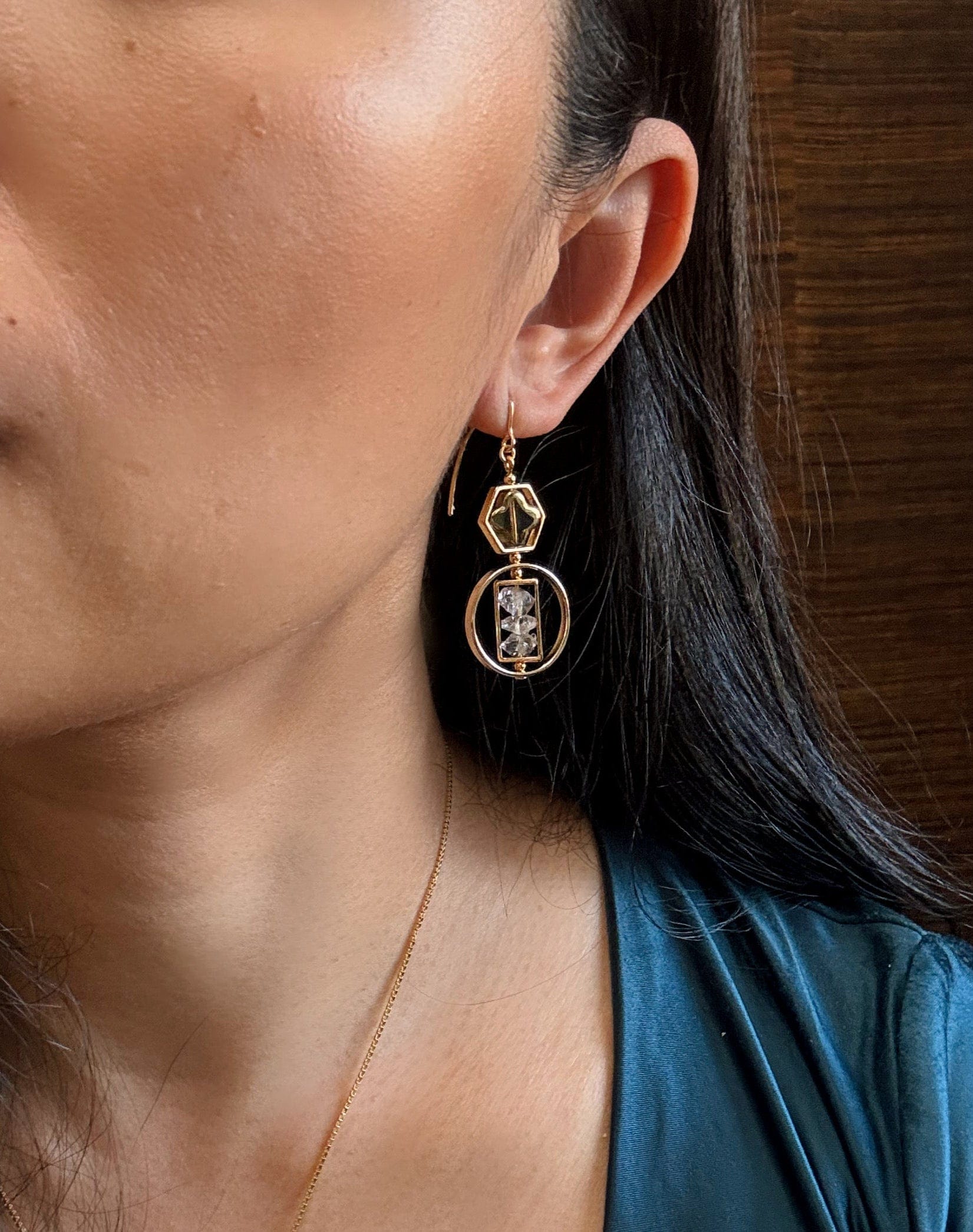 Close-up of a person wearing gold earrings and a matching necklace against a wooden background