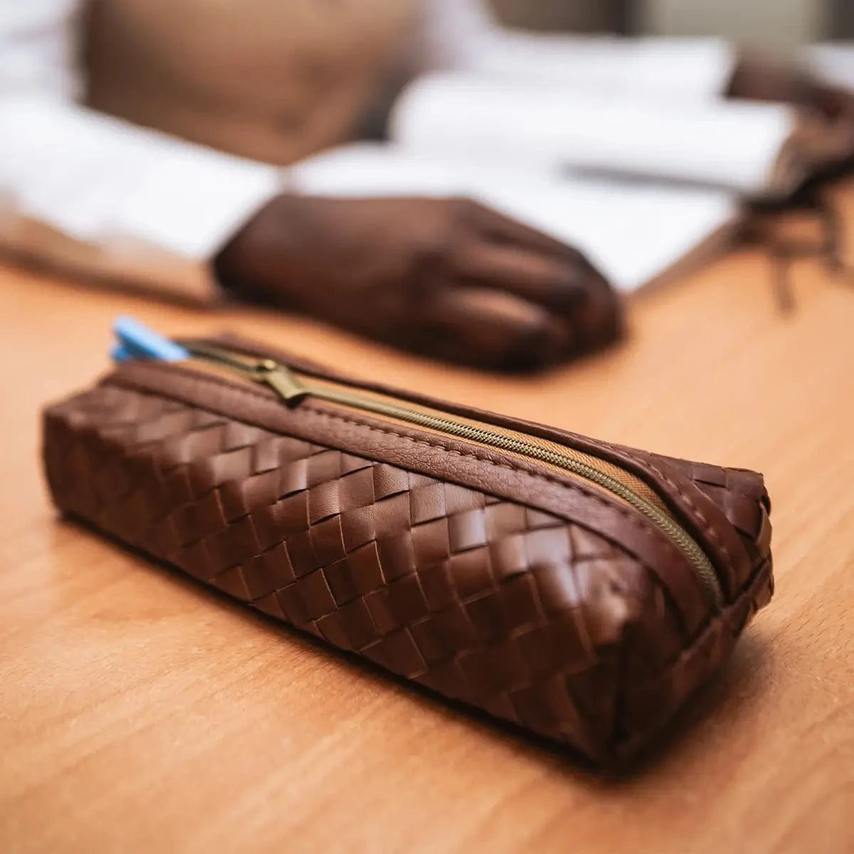 Brown woven leather pencil case on a wooden surface with a blurred background or artisan in factory