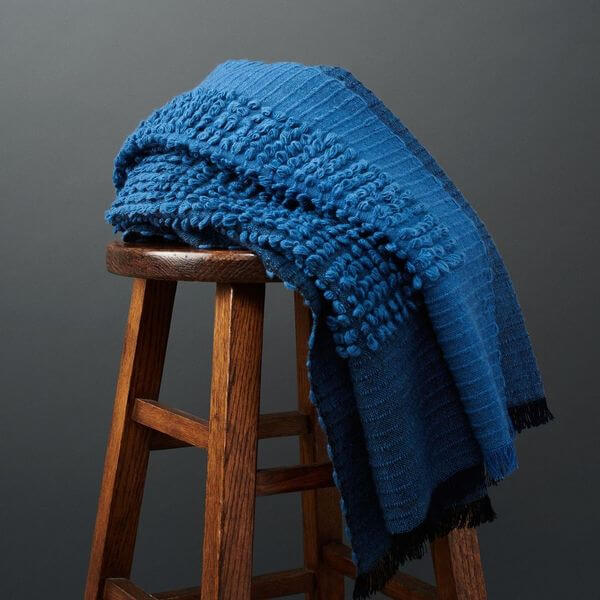 Macaroon Midnight Dark Blue Textured Merino Handloom Throw displayed on a wooden stool.