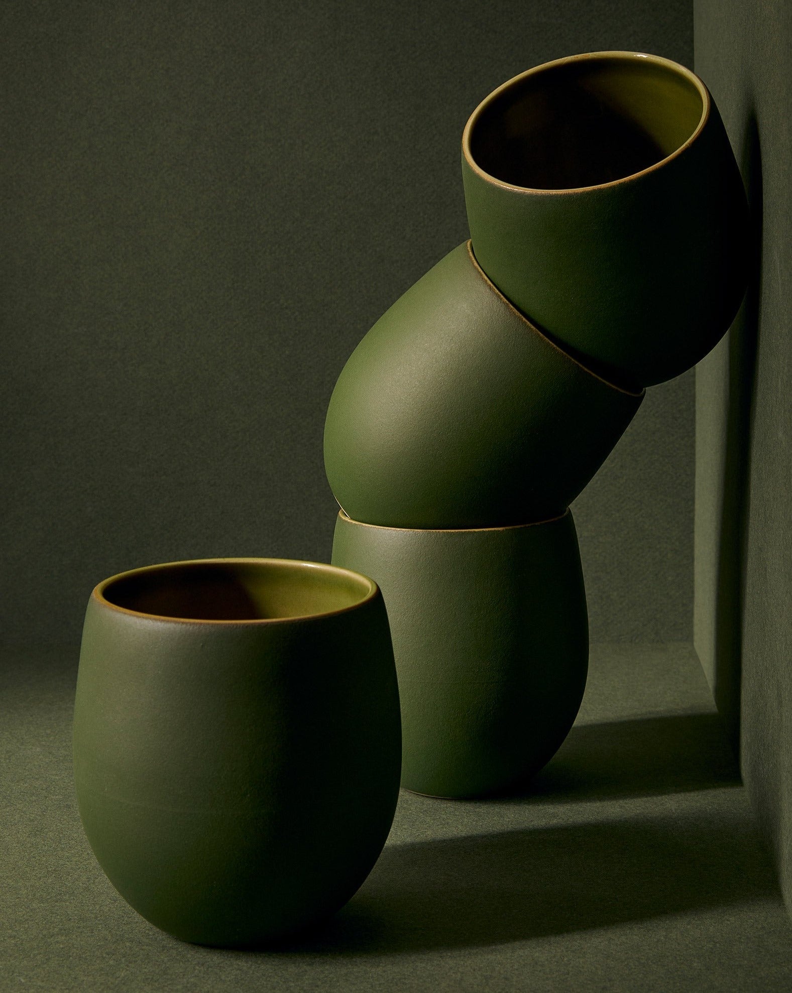 A set of beige stoneware coffee and tea cups with a matte finish, displayed in an artistic manner against a neutral background.