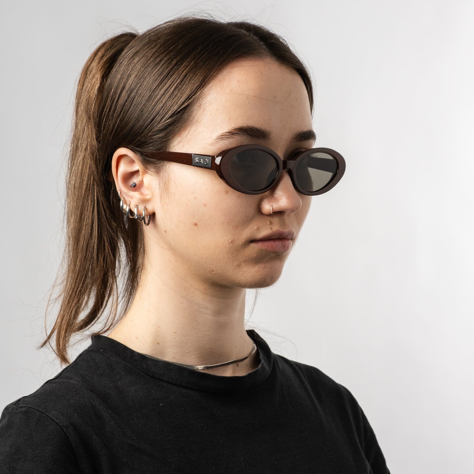 Female wearing Sad Eyewear Bloom oval sunglasses in tobacco red with tinted black lenses