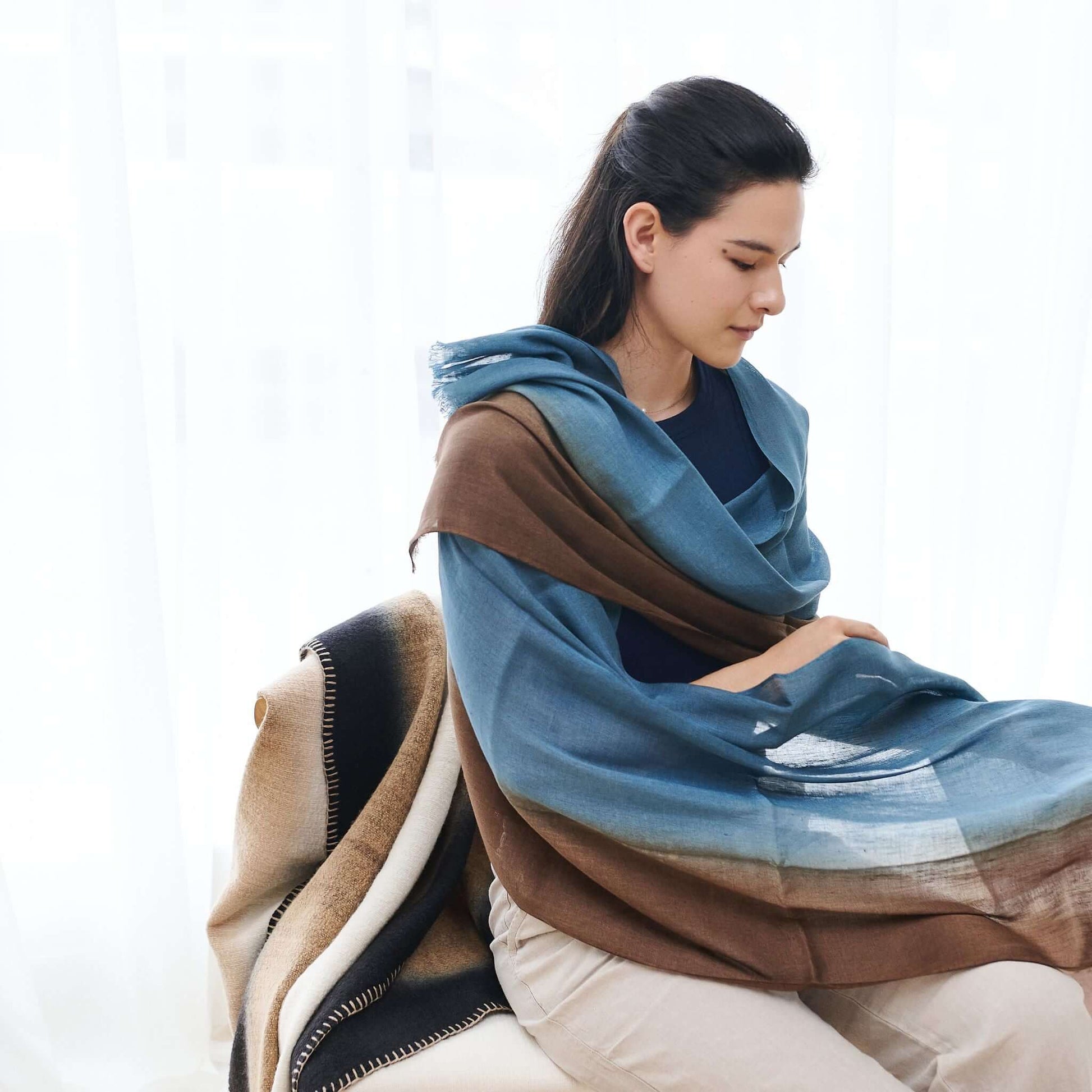 Mahogany Sky Brown Blue Ombre Linen Silk Handloom Scarf draped elegantly over a woman seated indoors.
