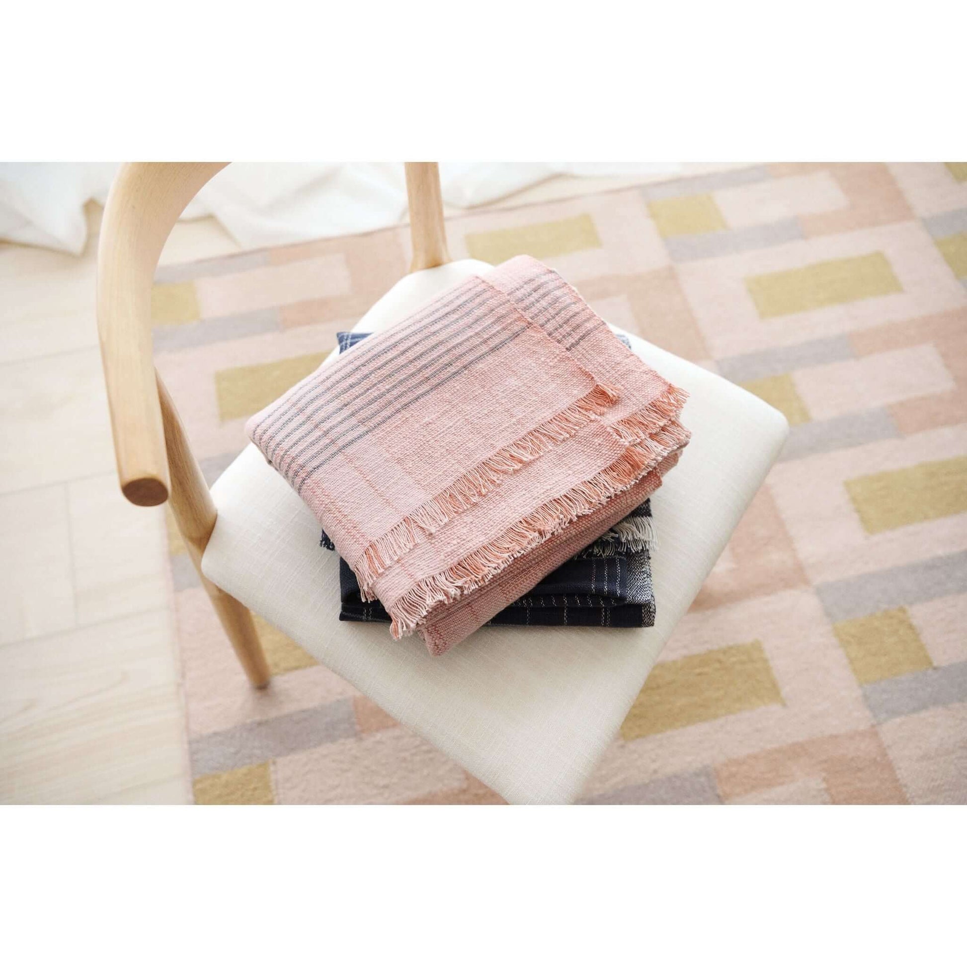 Silica Rose In Shades of Salmon Pink Gray Stripes Pattern Soft Handwoven Merino Throw draped on a chair.