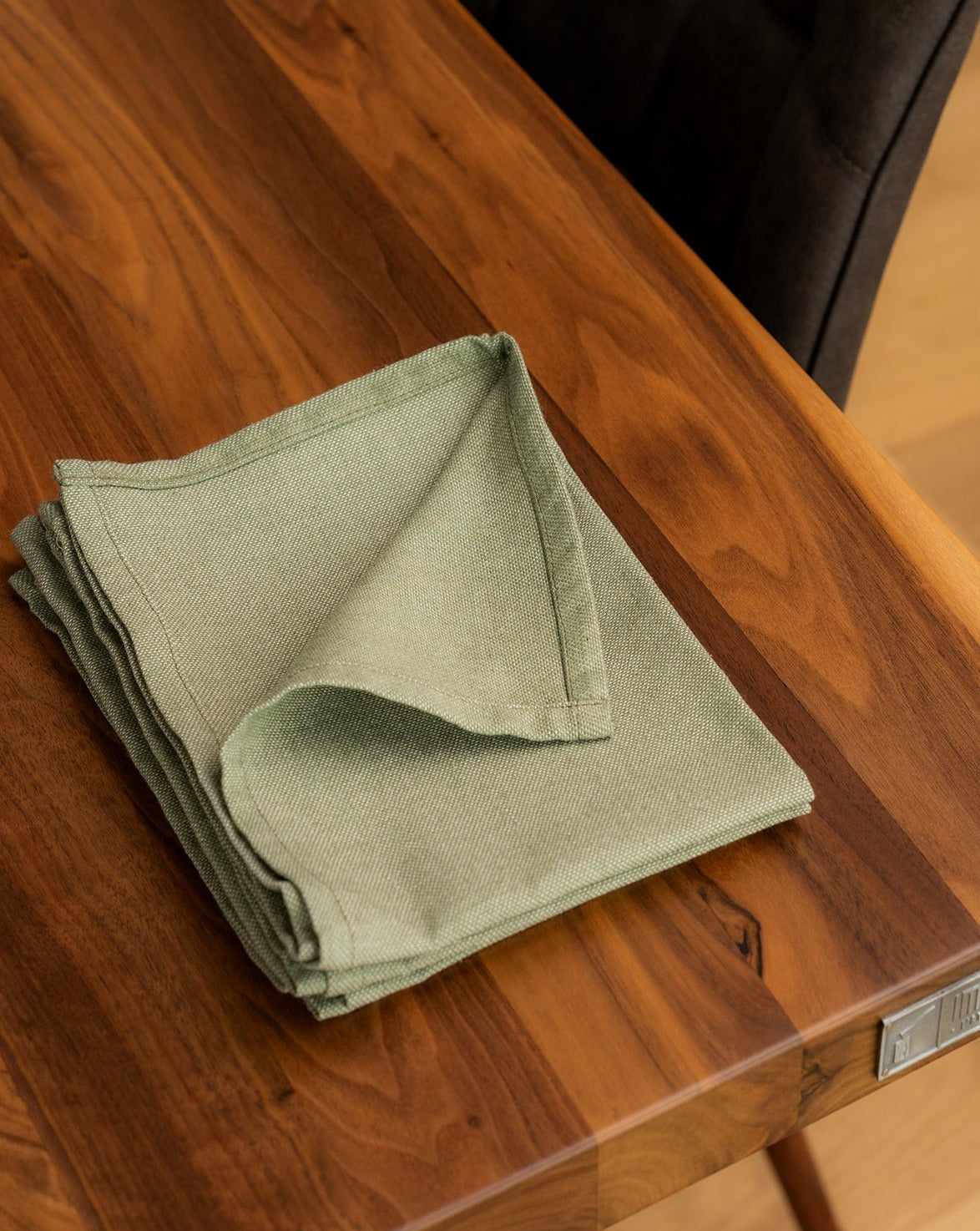 A folded Green cotton napkin on a wooden dining table