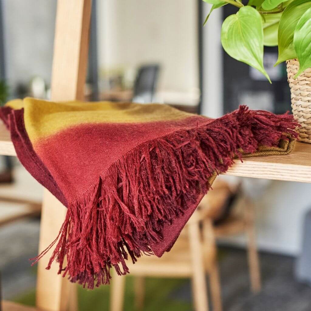 Marigold Merino Ombre Handloom Throw / Blanket Scarf draped on a wooden shelf showcasing its vibrant ombre colors and fringes.