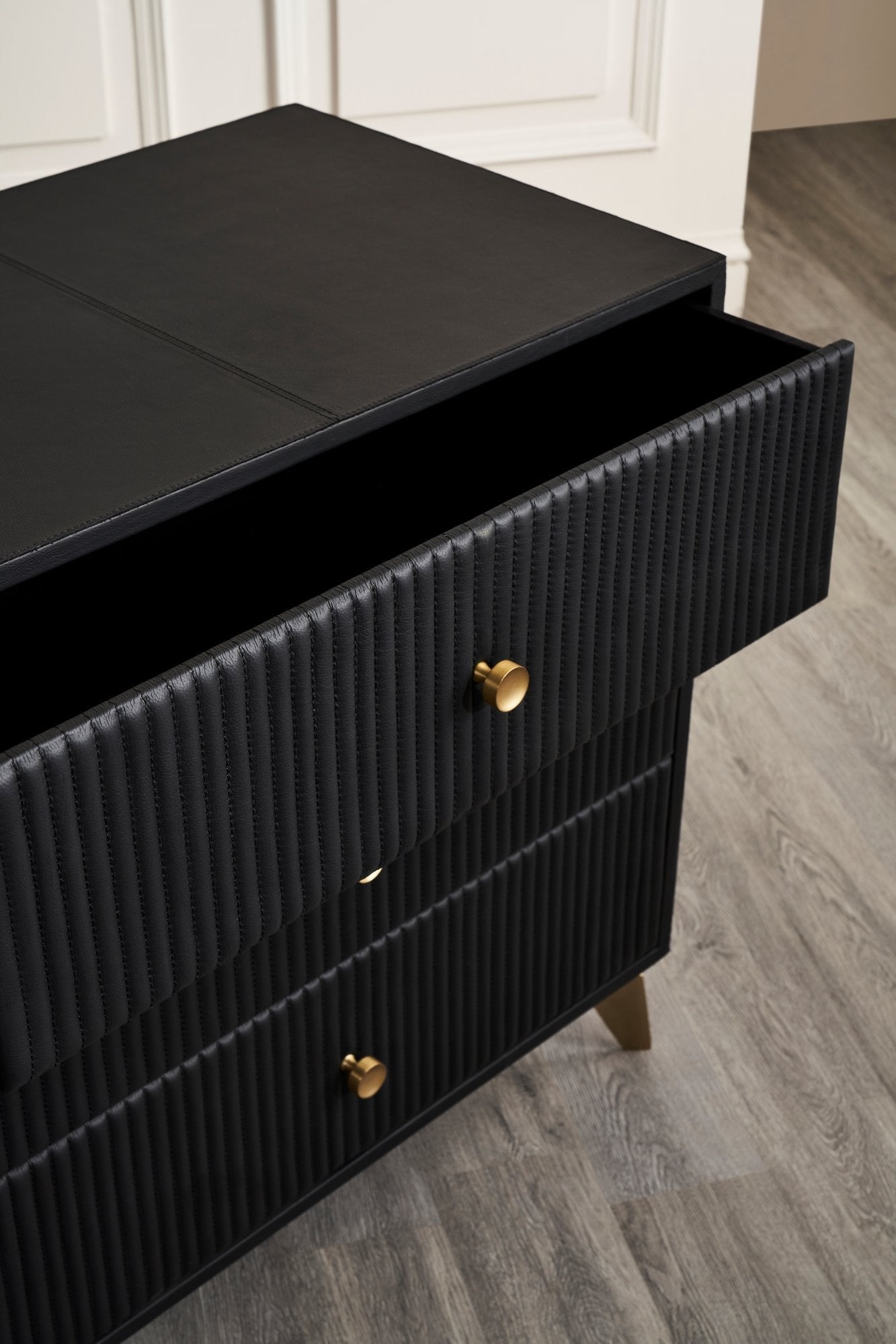 FN-5202-262028_7|Detailed black leather 3-drawer nightstand with top drawer open, highlighting vertical channel tufting and elegant golden knob. Premium furniture.