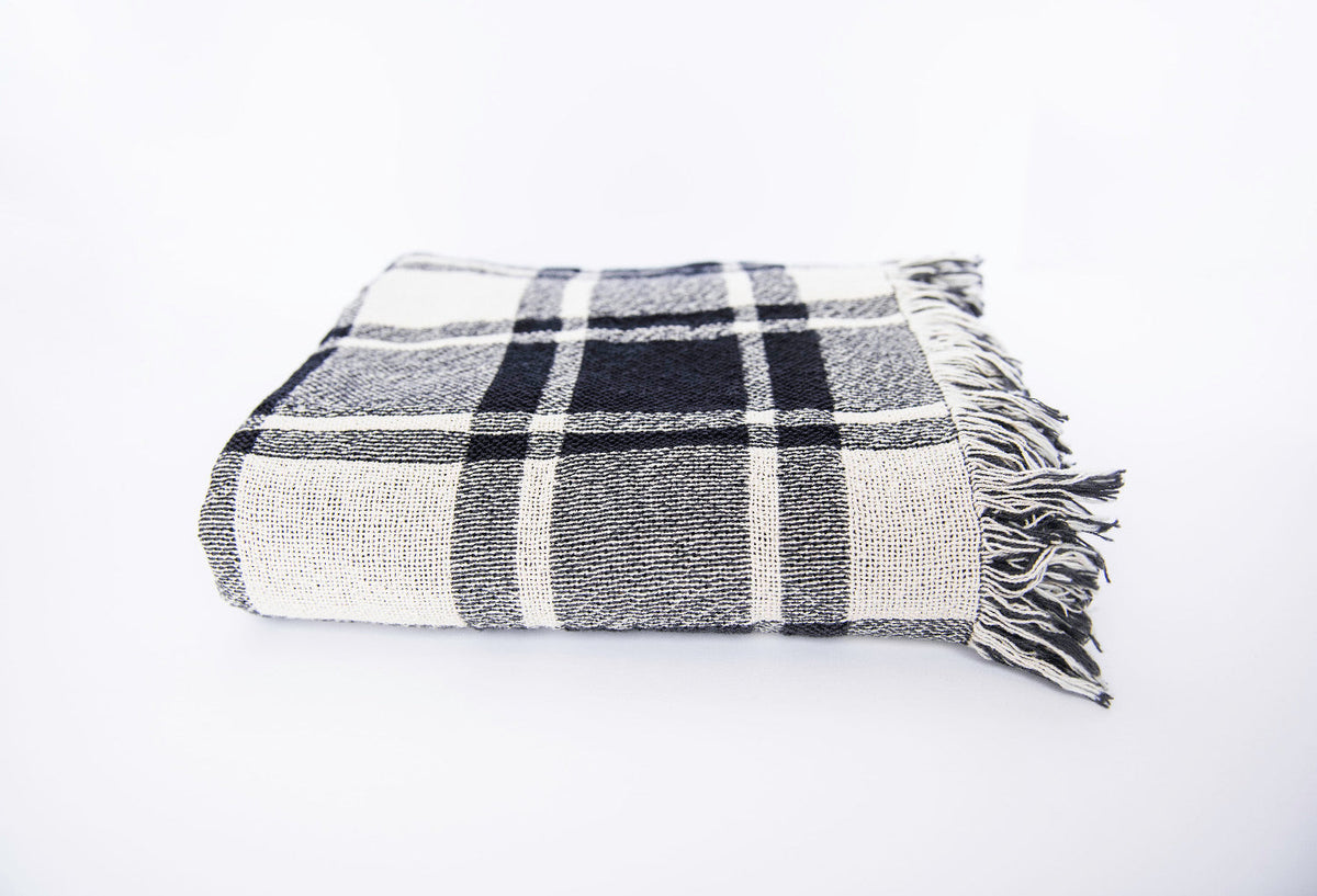 Front view of folded black, gray, and cream plaid woven cotton throw on a white background