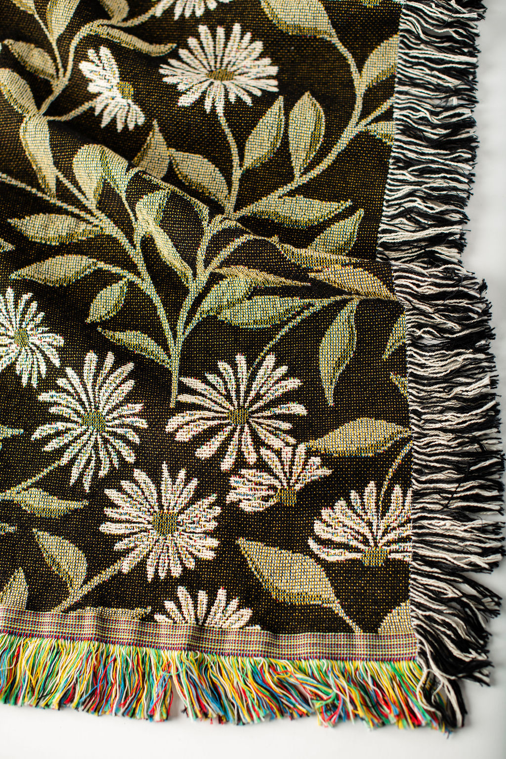 Close-up of May Bramble black, gold, green, and cream floral botanical jacquard woven blanket with fringe
