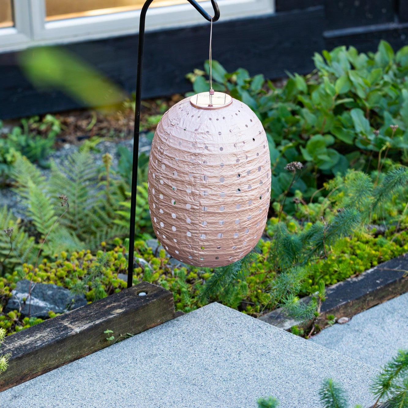Beige hanging lantern on a stand in a garden setting