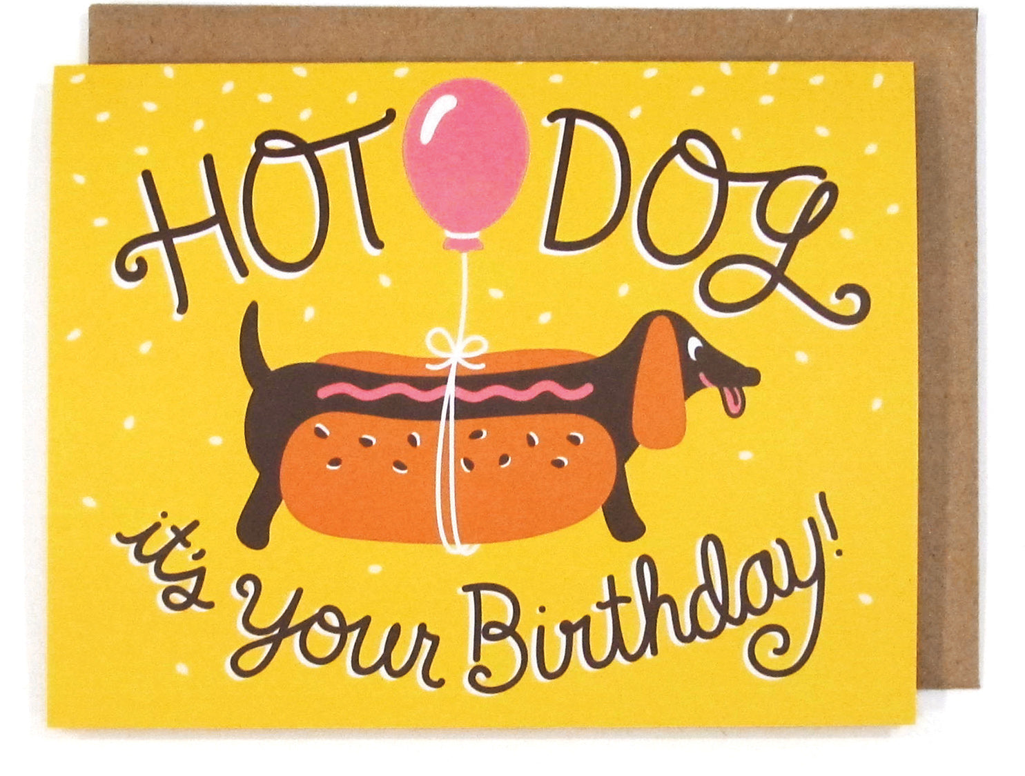 Yellow card that pictures a dachshund ina  hot dog costume with a ballomn tied around its belly, featuring the phrase "Hot dog it's your birthday!," with a brown envelope