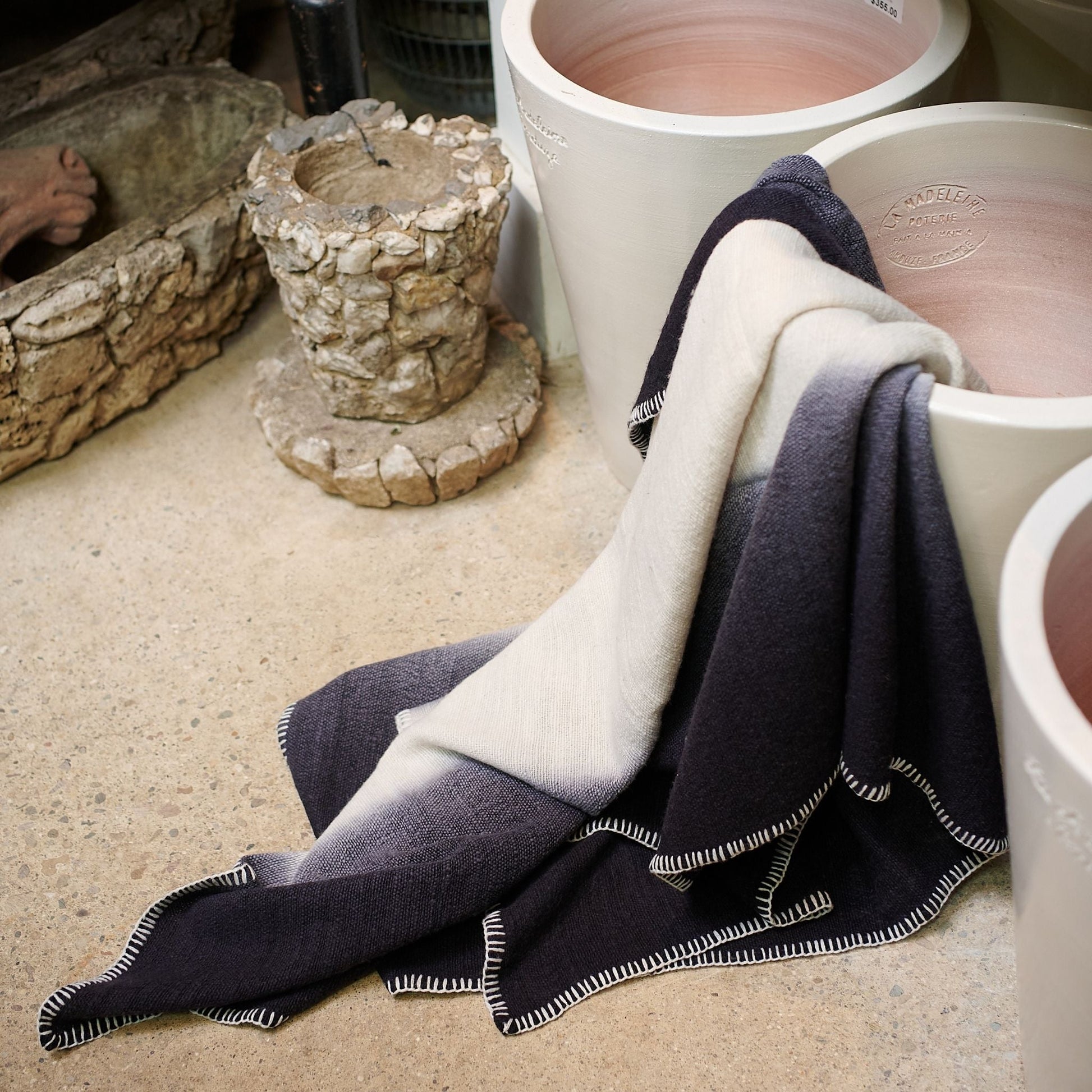 Ink Black White Ombre Textured Throw  In Hand Spun Merino And Hand Stitched Hem draped over pottery in a serene setting.
