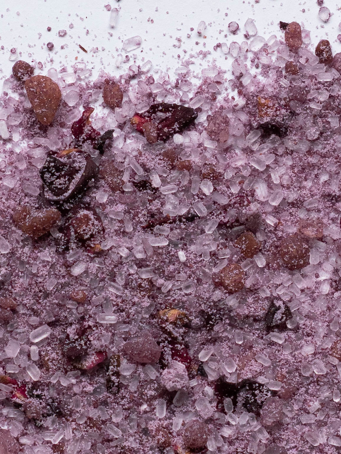 Close-up of pink salt with small pink rose petals on a white background.