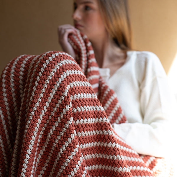 Person wrapped in a red and white striped organic cotton throw against a neutral background.
