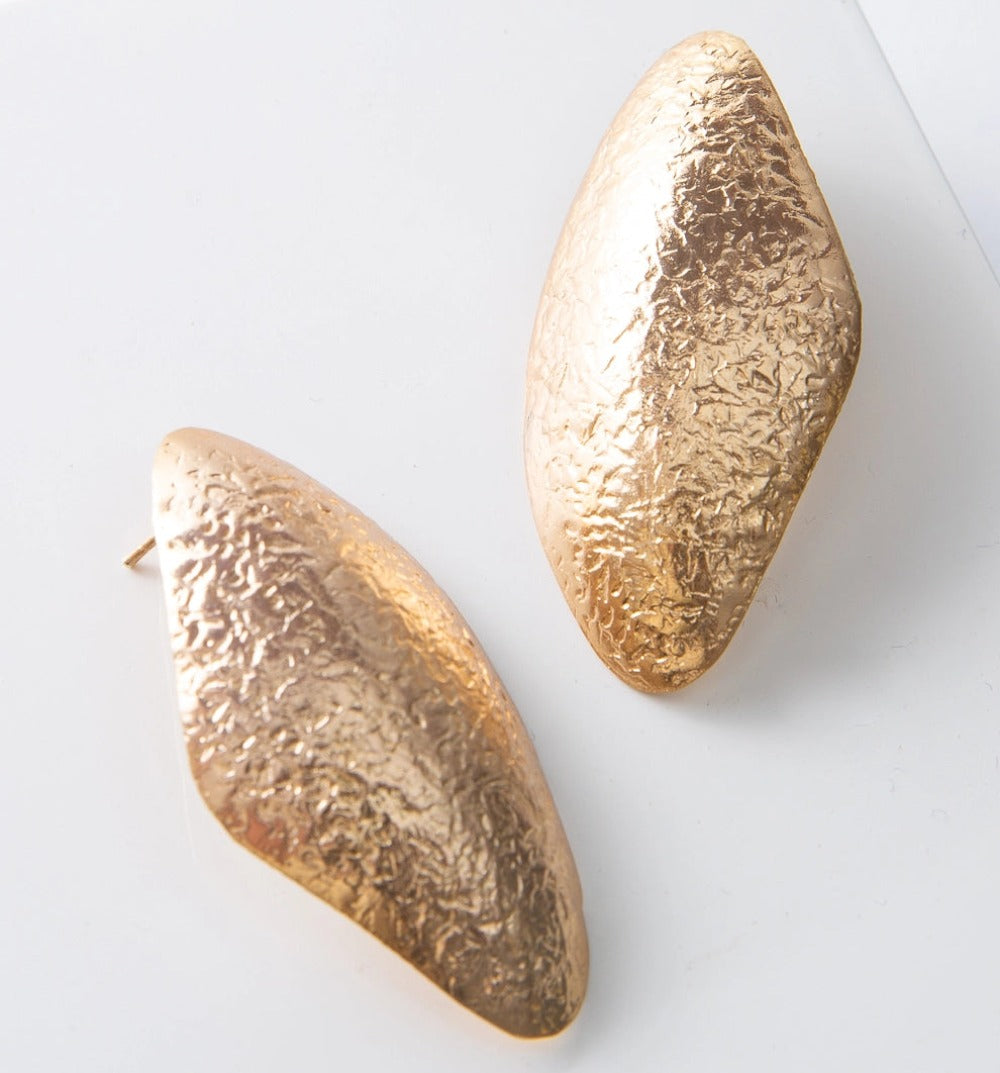 These are post-style earrings composed of shining gold-plated brass with a hammered texture. The earrings have an irregular, organic look and are roughly diamond shaped, with smooth rounded edges.