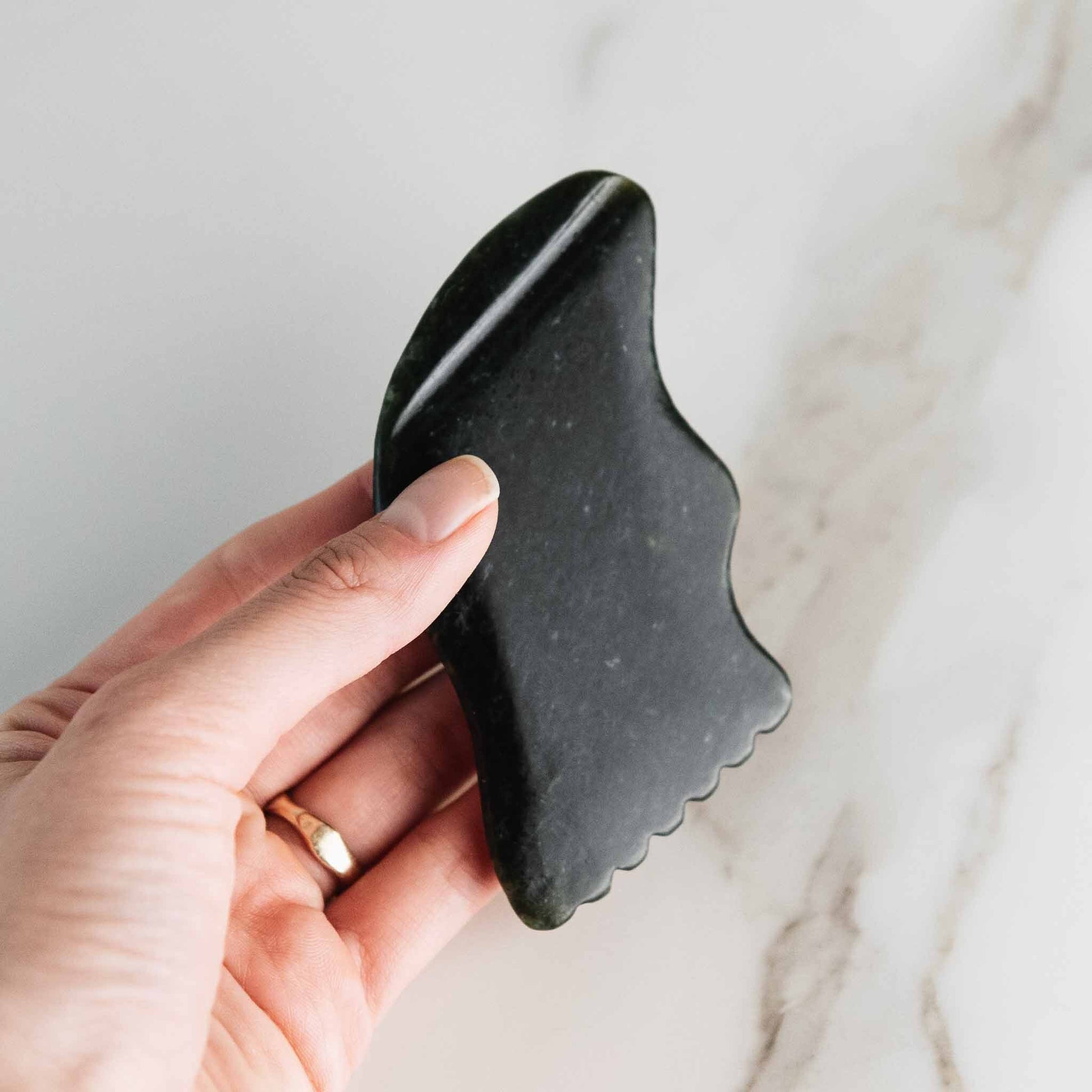 Hand holding a black gua sha facial massage tool used for sculpting, lymphatic drainage, and promoting circulation in skincare routines