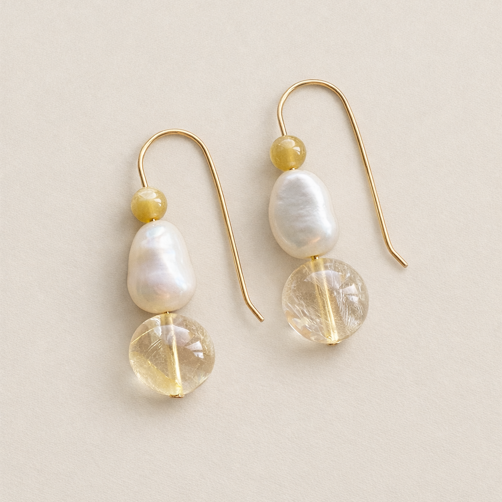 Pair of earrings with gold and pearl-like beads on a beige background