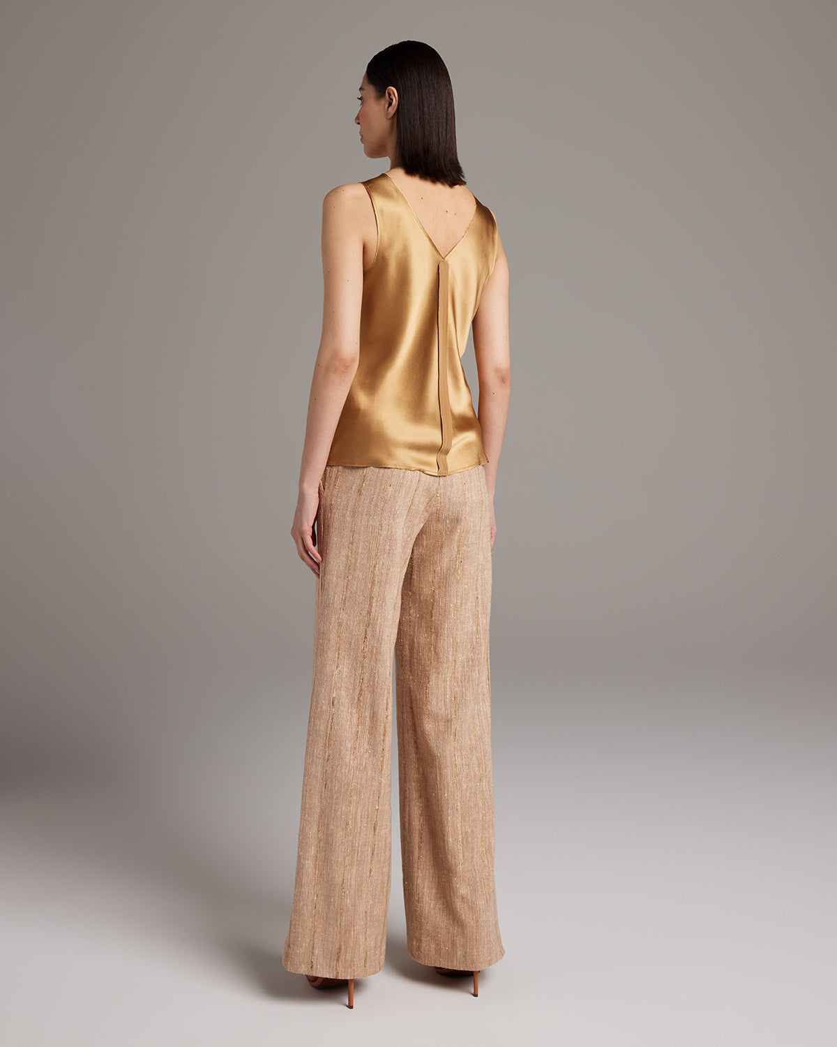 Model wearing a gold silk raw edge tank top and beige palazzo pants from the back