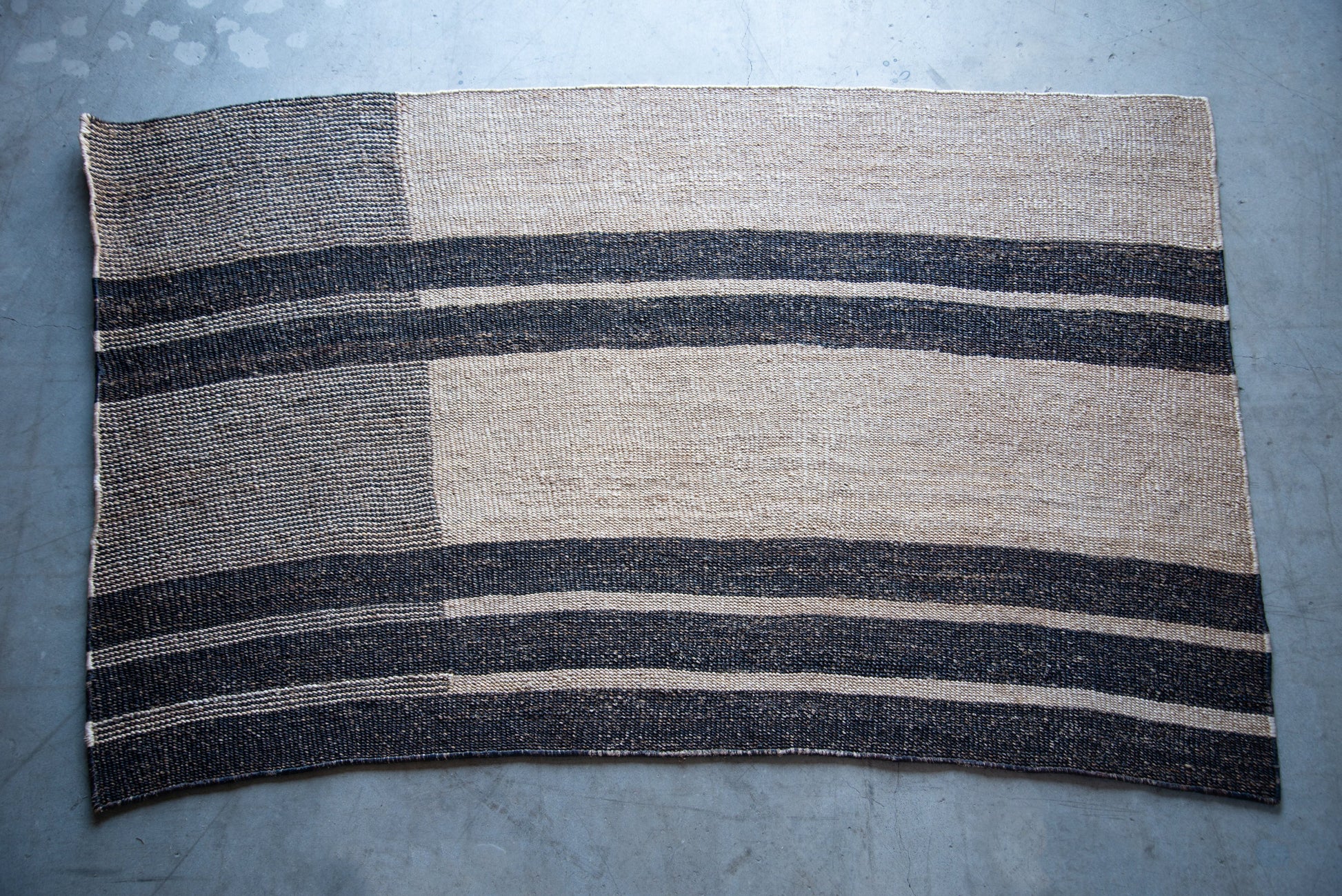 A rectangular sisal rug in a room with a fireplace, sofas, and wooden beams on the ceiling.