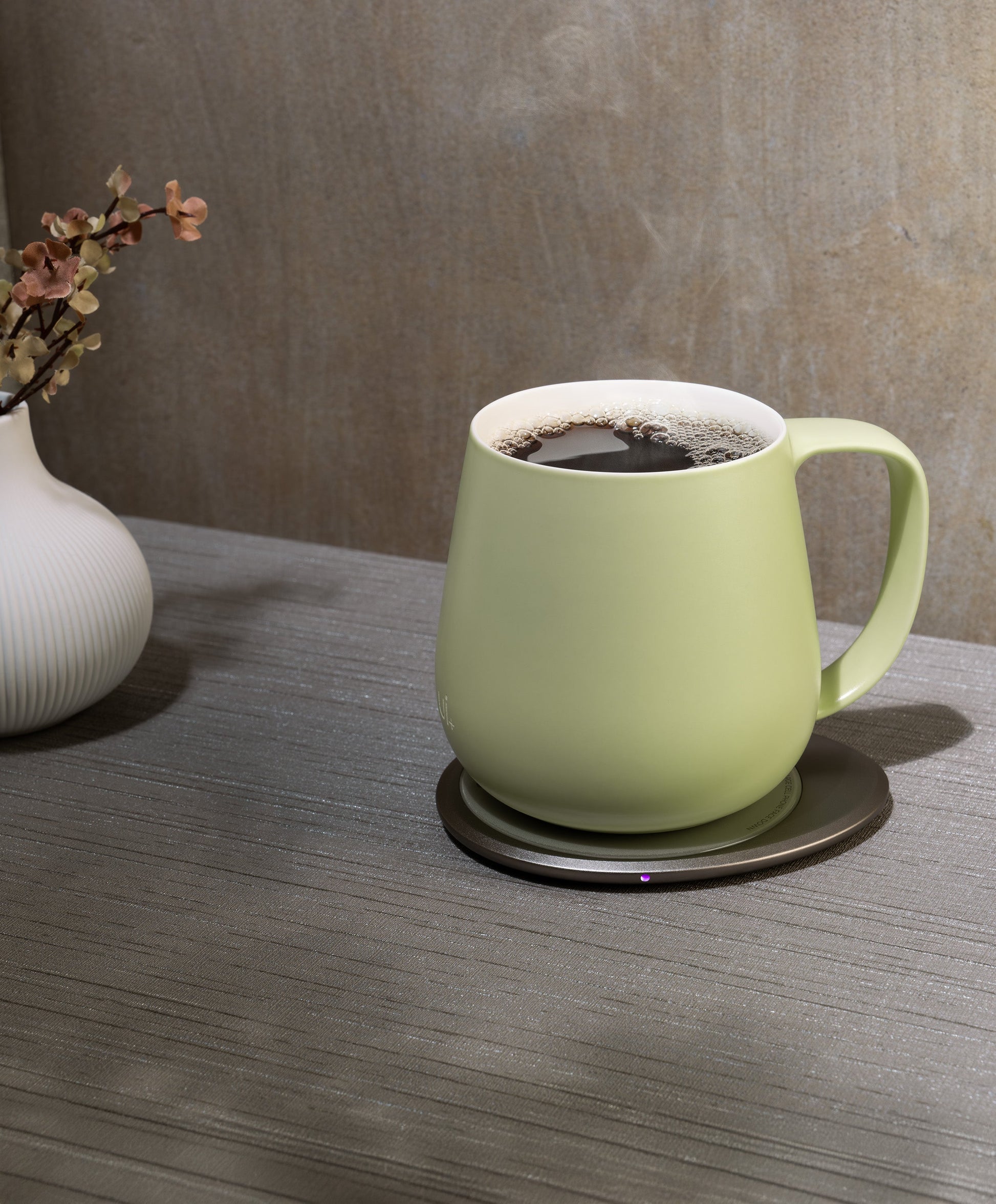 Ui+ self-heating ceramic mug set 18 fl oz / 532 mL in Verde Green charging on OHOM Pad 3, filled with hot coffee and steam rising
