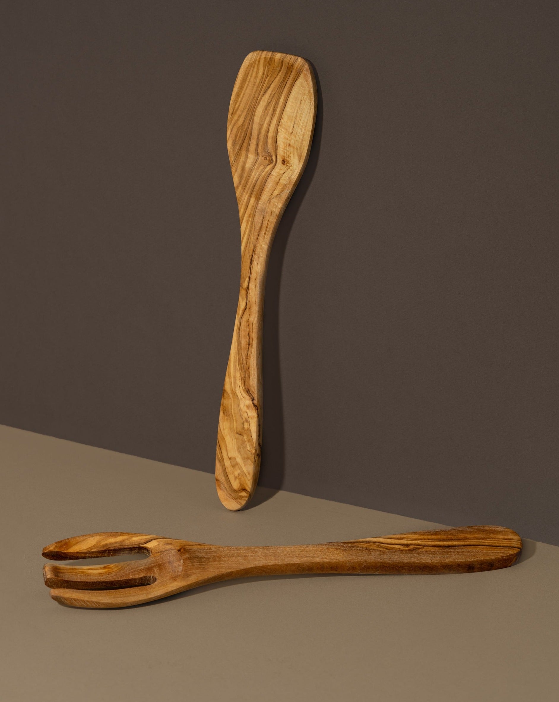A wooden spoon and fork set made of olivewood, displayed against a dark background.