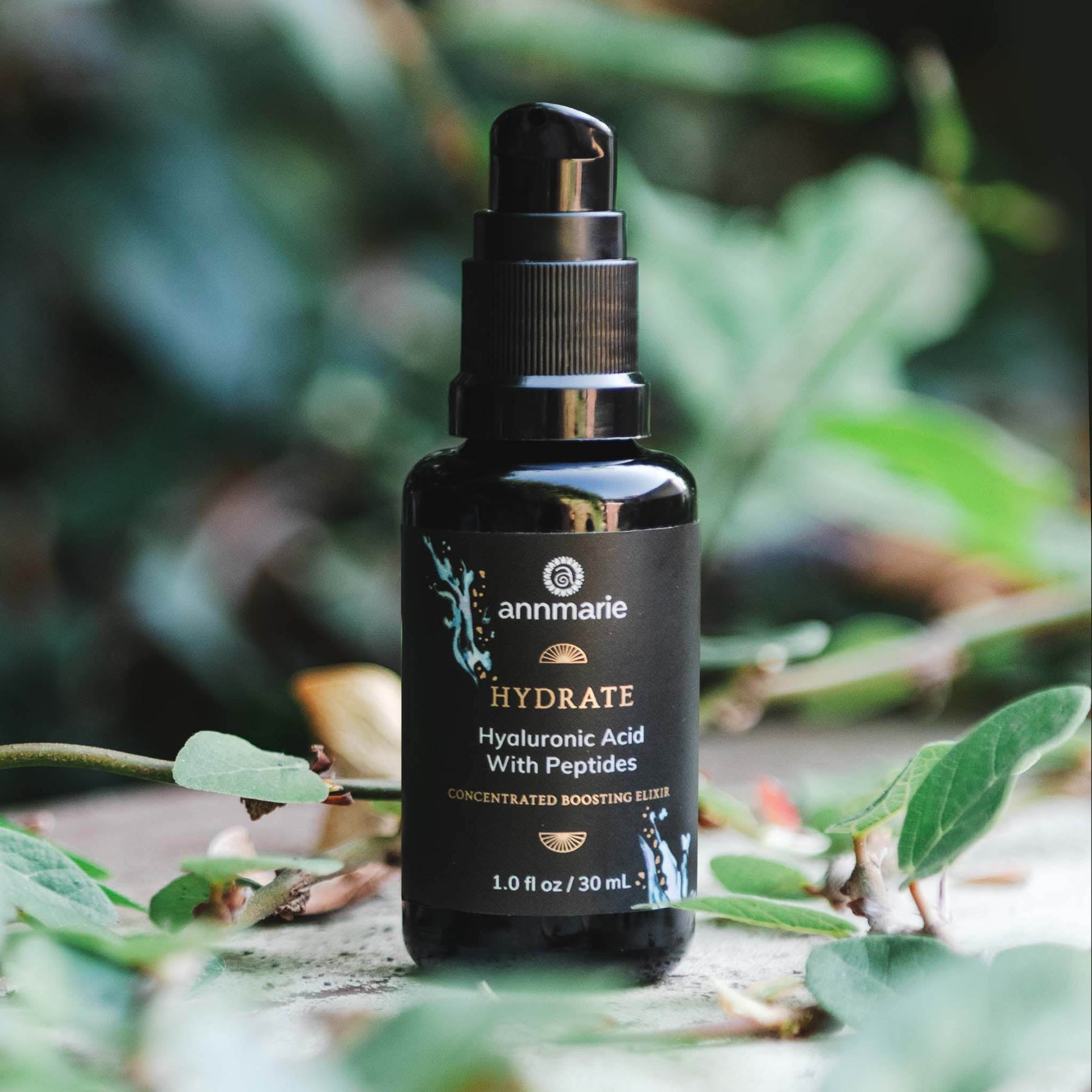 Hydrate Hyaluronic Acid with Peptides concentrated boosting elixir in a dark glass pump bottle surrounded by natural greenery.