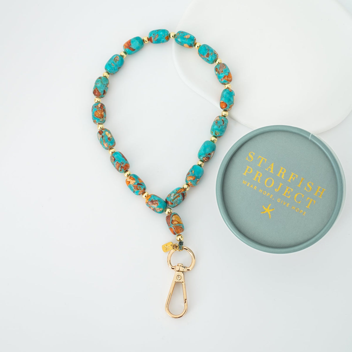 Sierra Bloom turquoise beaded wrist strap with gold clasp beside a Starfish Project box lid