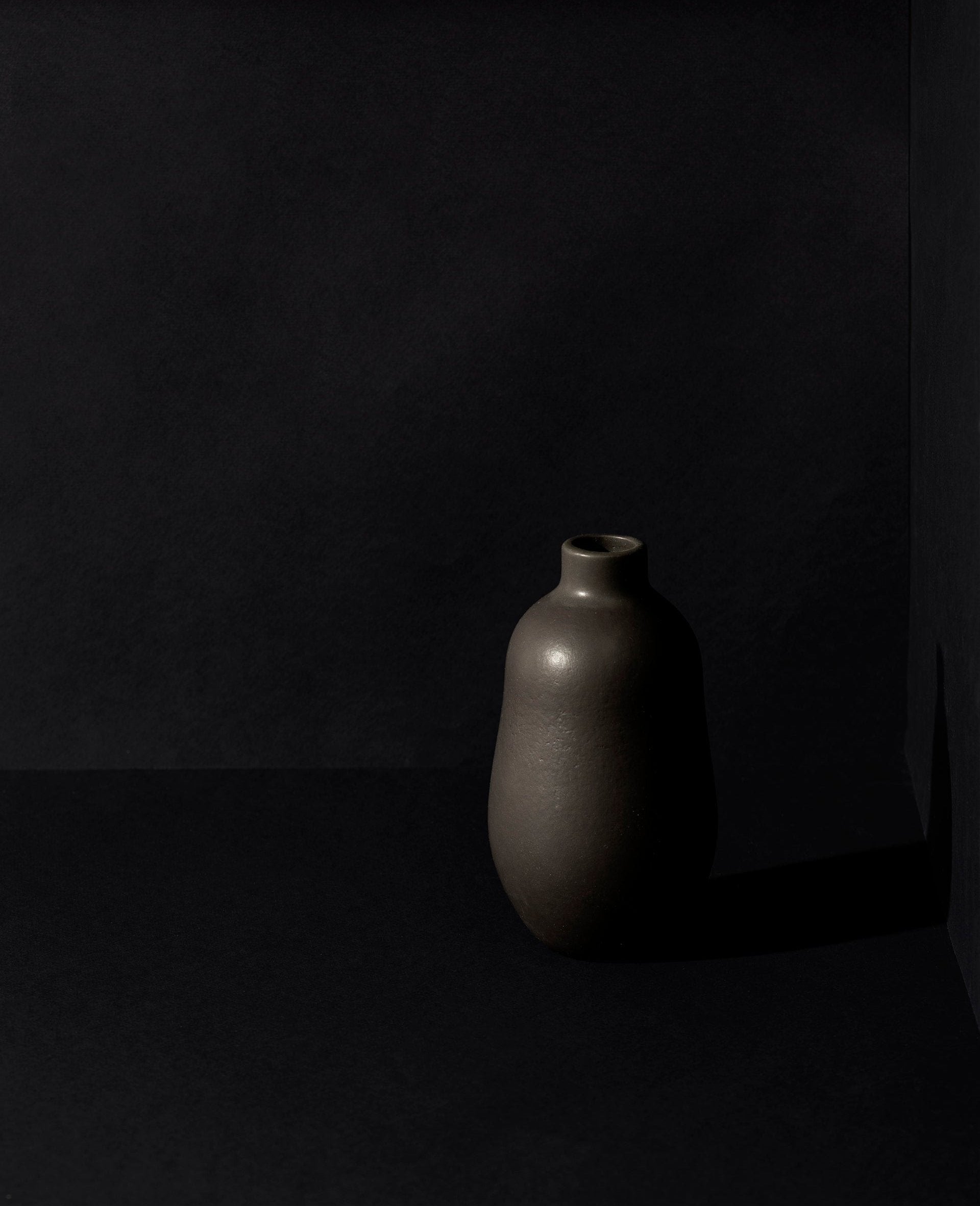Matte black handmade enameled stoneware vase with a minimalistic and ethno-contemporary design, set against a dark background to highlight its smooth matte finish.