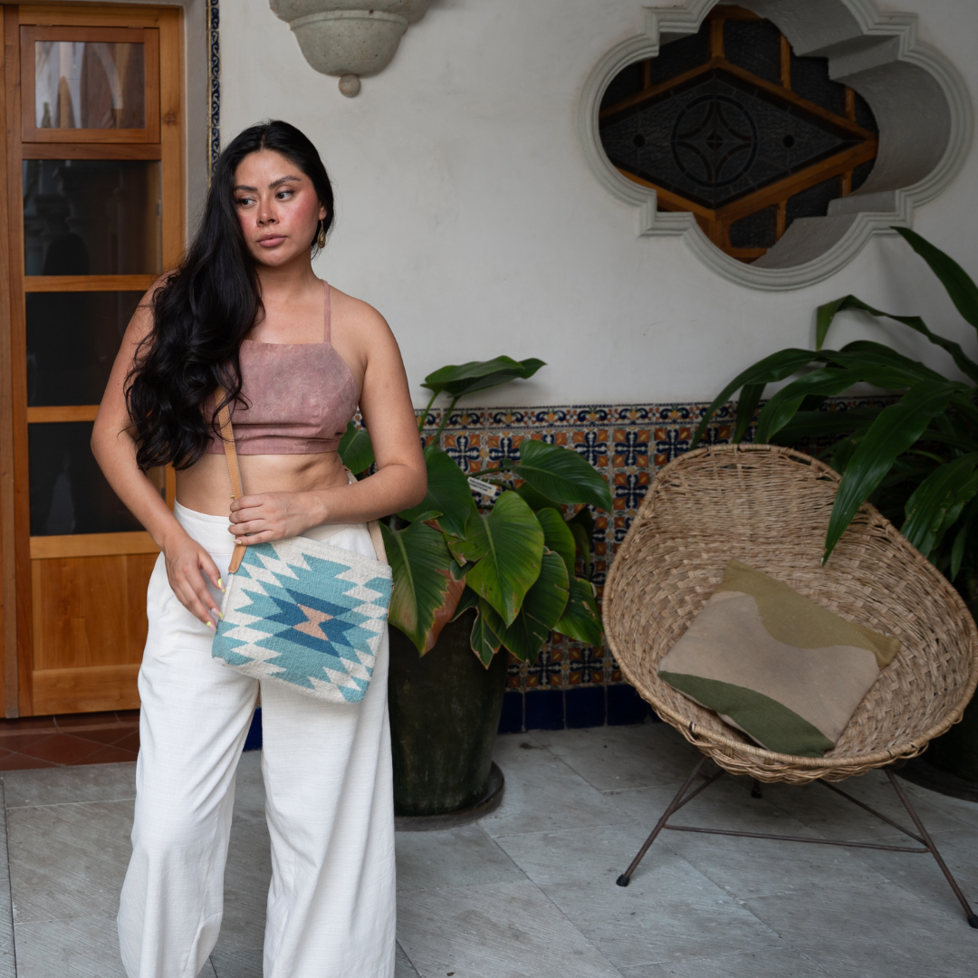 Woman carrying handwoven crossbody bag with abstract Zapotec diamond design in soft spring tones; features adjustable leather strap and two internal pockets for daily essentials