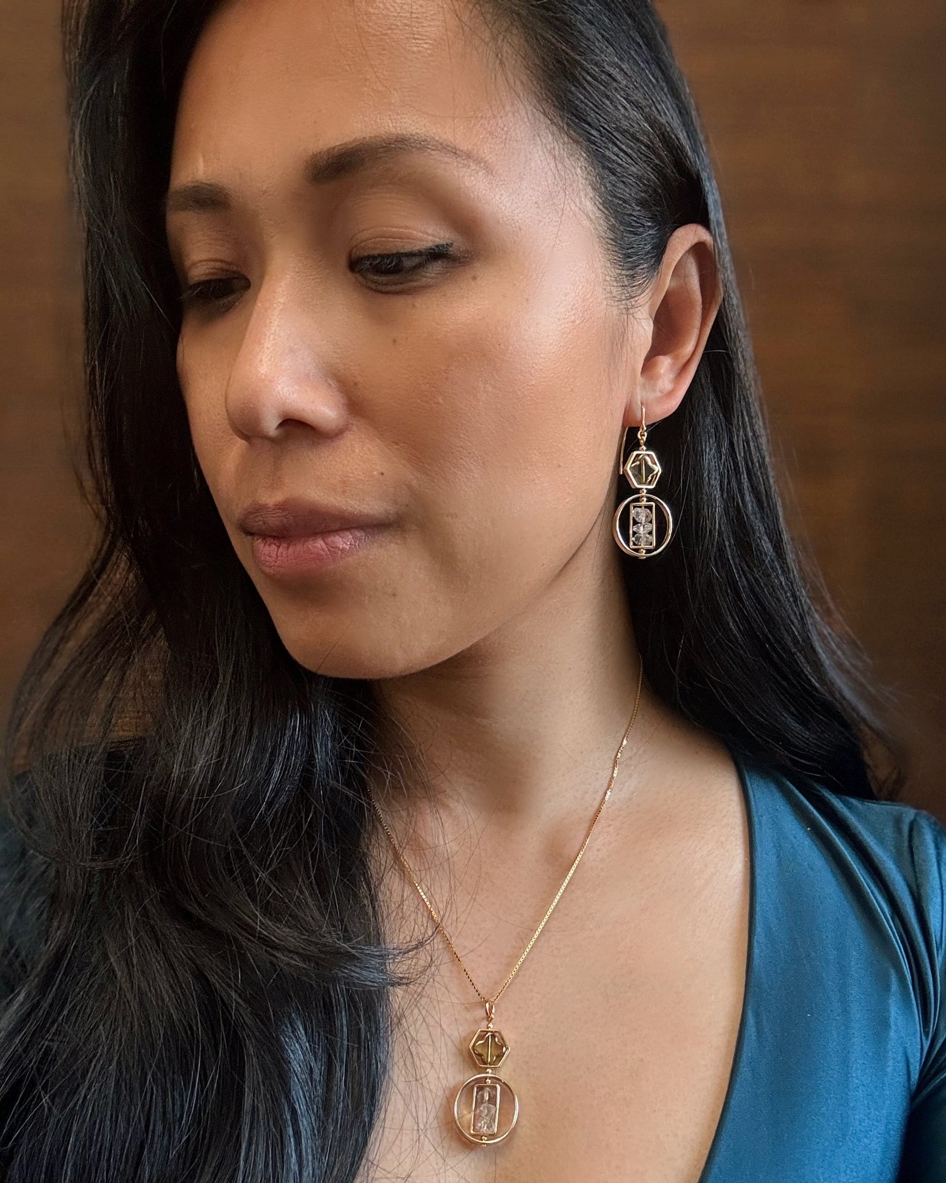 Woman wearing gold earrings and necklace against a brown background