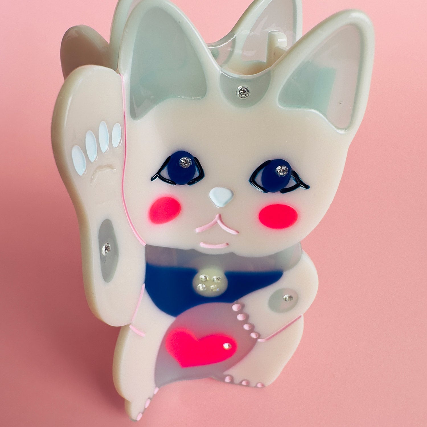 A maneki-neko white cat hair claw with a pink heart from Centinelle. Handmade on cellulose acetate, with splice technique, exquisite miniature details and crystals, that are tied directly to its value and make them unique and special. 