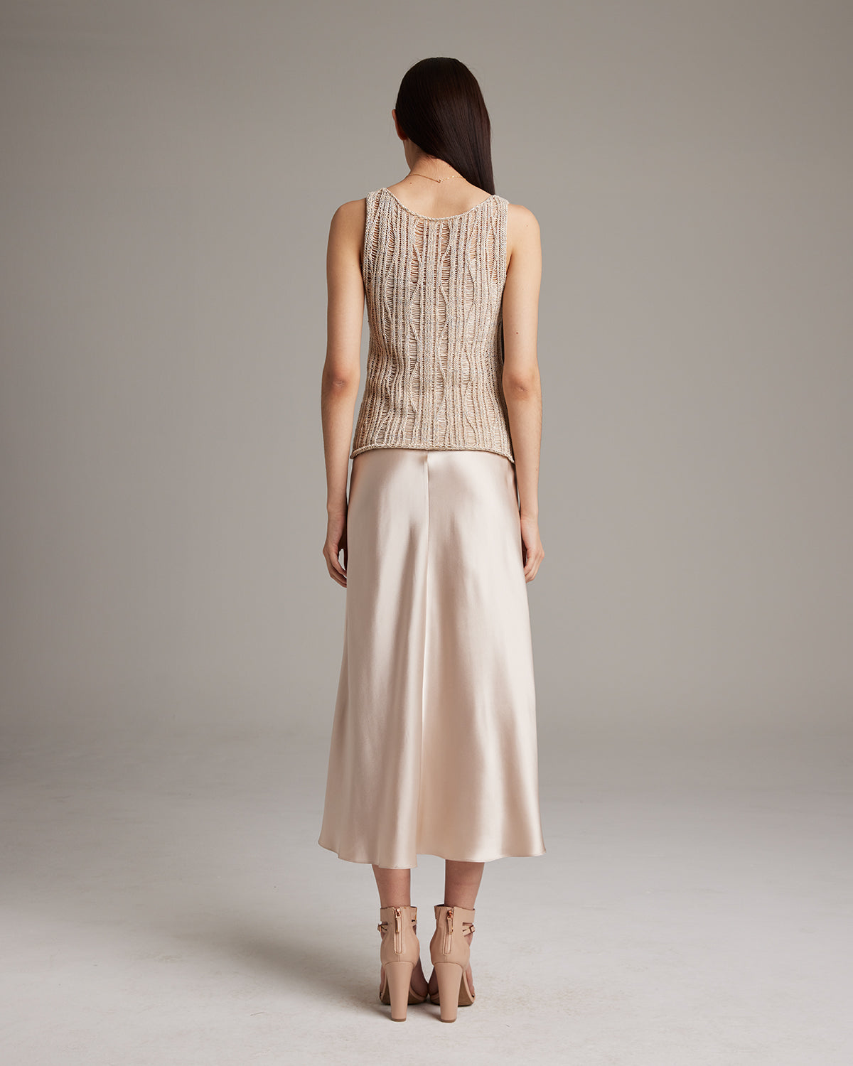 Model wearing a lace knit tank top from the back, paired with a satin skirt.