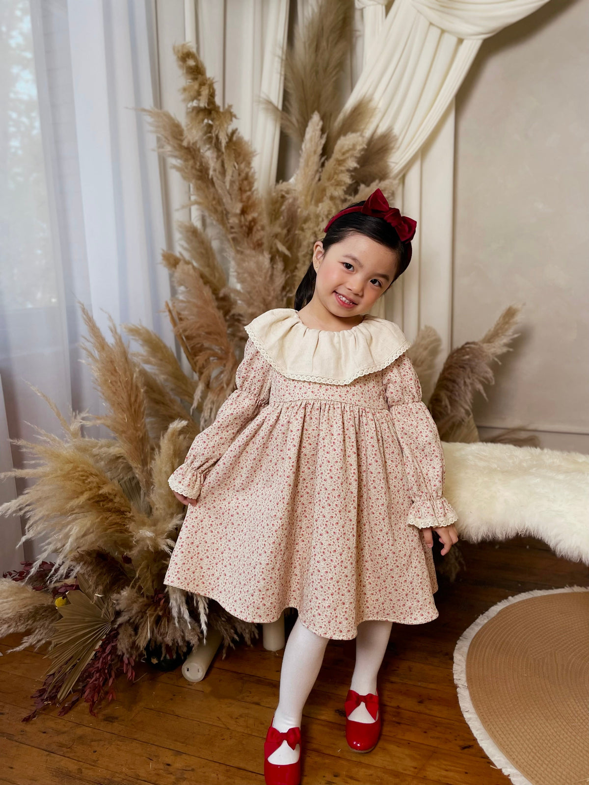Young girl in a floral dress with pampas grass and white curtains in the background