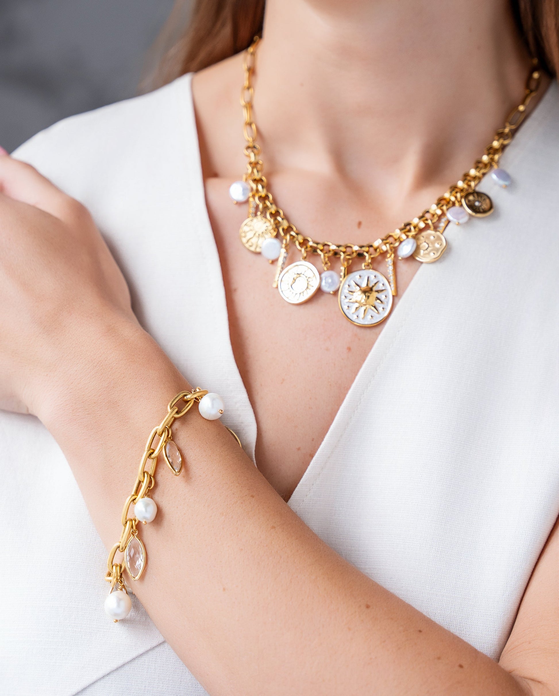 Gold celestial charm necklace with sun medallions, coin pearls, pavé crystal accents, and dangling celestial charms on a chunky chain.