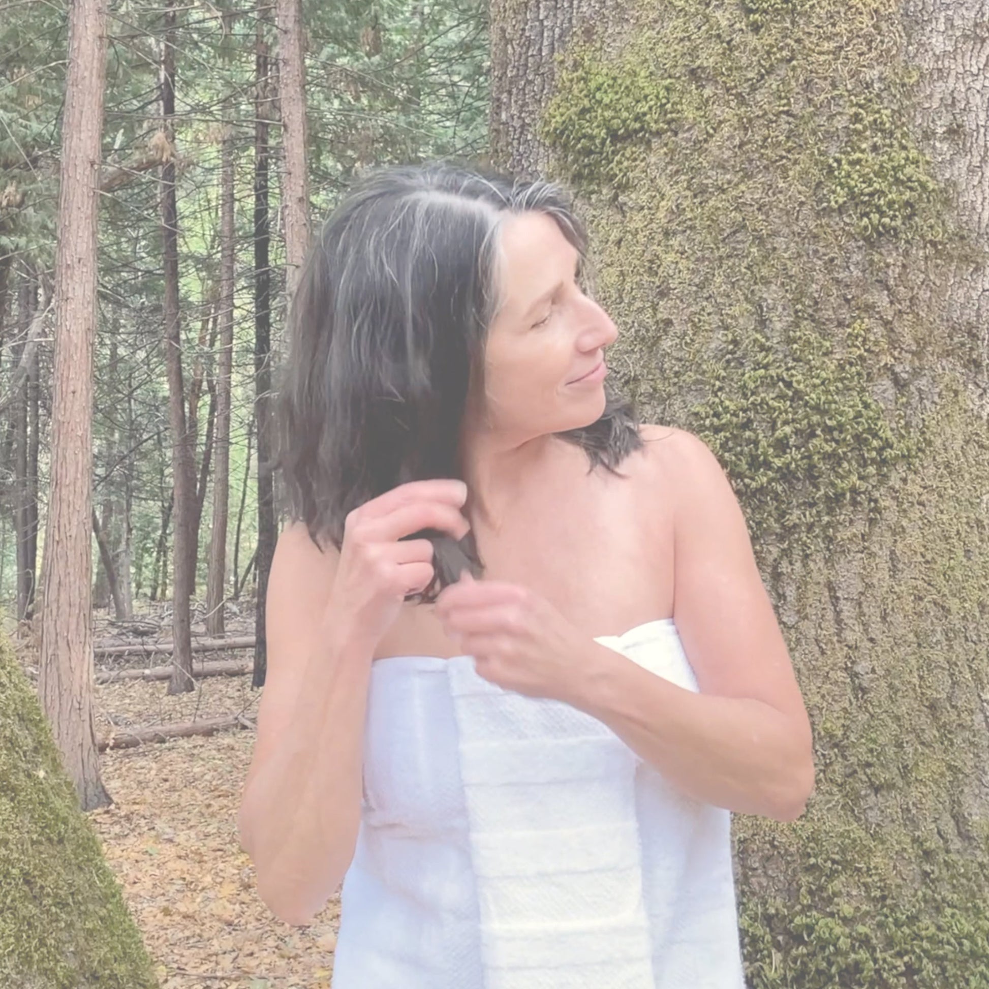 Video of woman outdoors in a forest applying smoothing hair serum to the ends of her hair, demonstrating how to use the product for soft, frizz-free results.