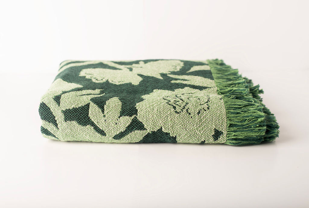 Front view of folded dark green and light green floral woven cotton throw on a white background