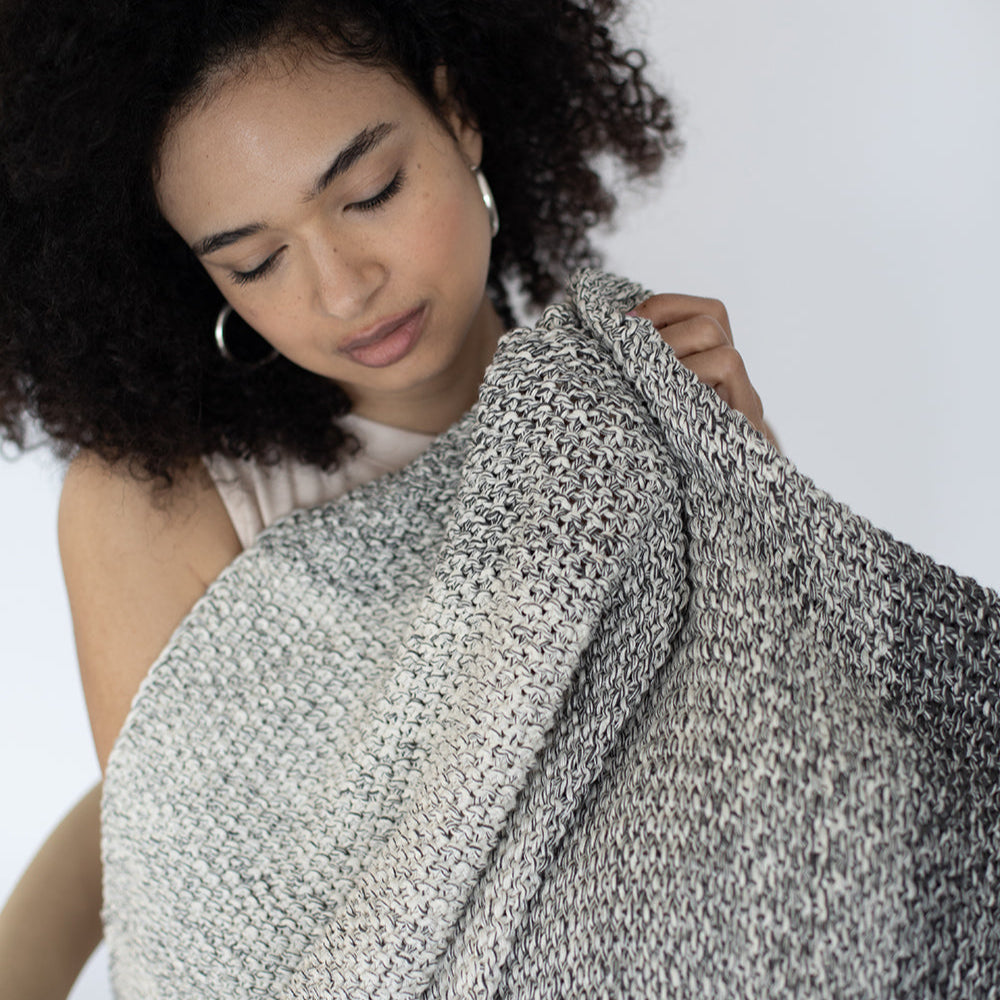 Woman holding a textured grey and ombre cotton throw against a white background.