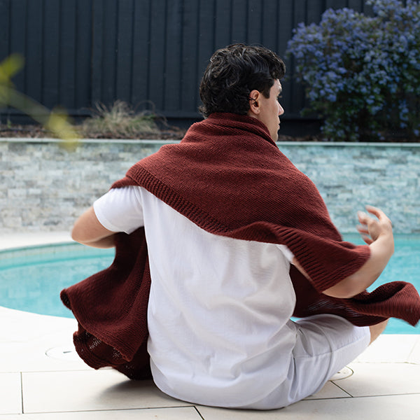 Man sitting on the pool side with a sagria brown knitted cotton throw draped over their shoulders.
