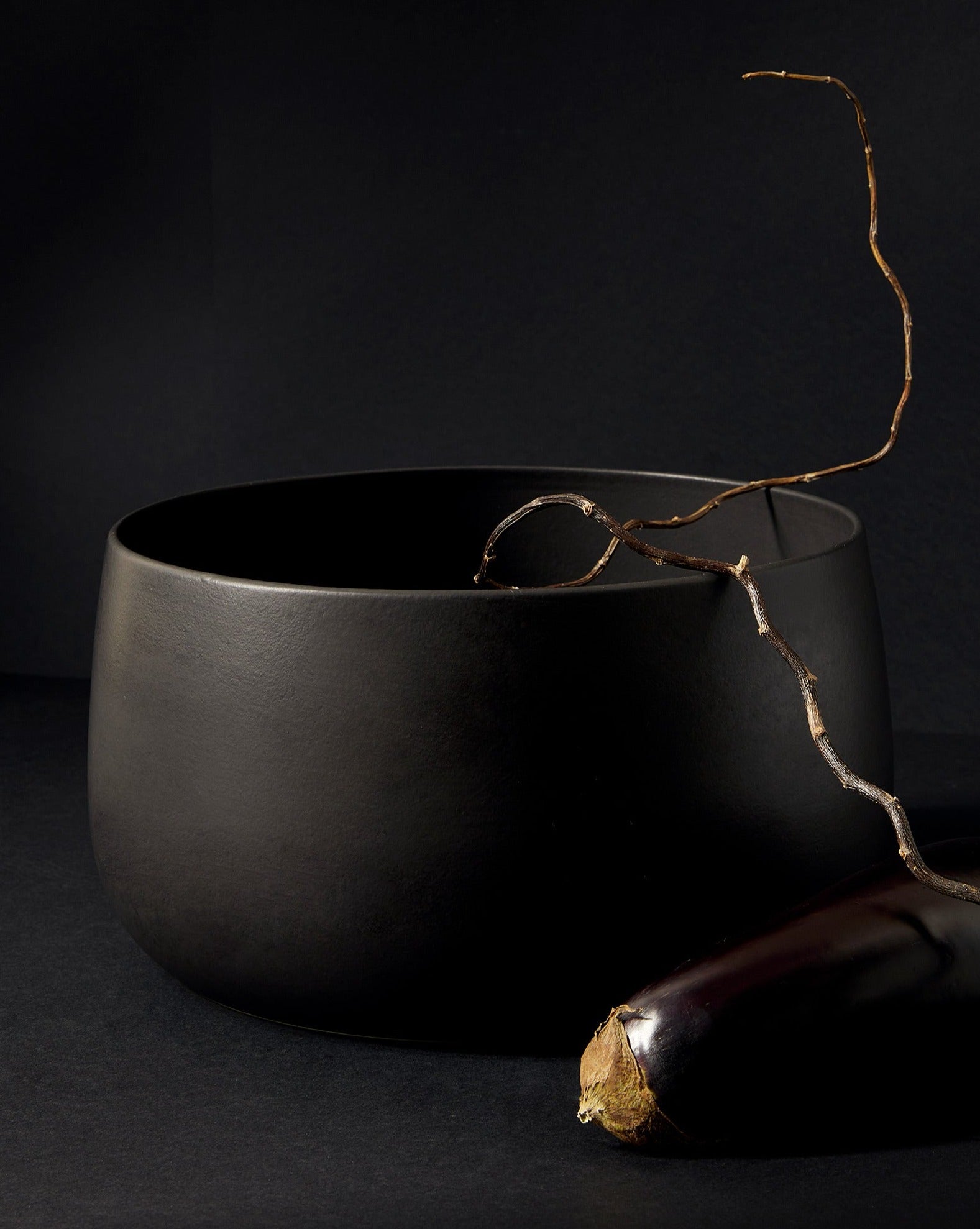 A large white stoneware serving bowl with a minimalist design, accompanied by two onions, presented against a neutral background.