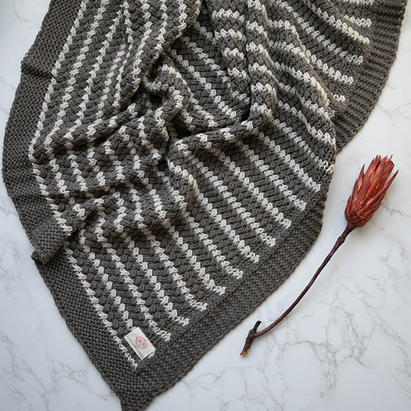 Knitted dark brown and white patterned cotton throw with a single red flower on a marble surface.