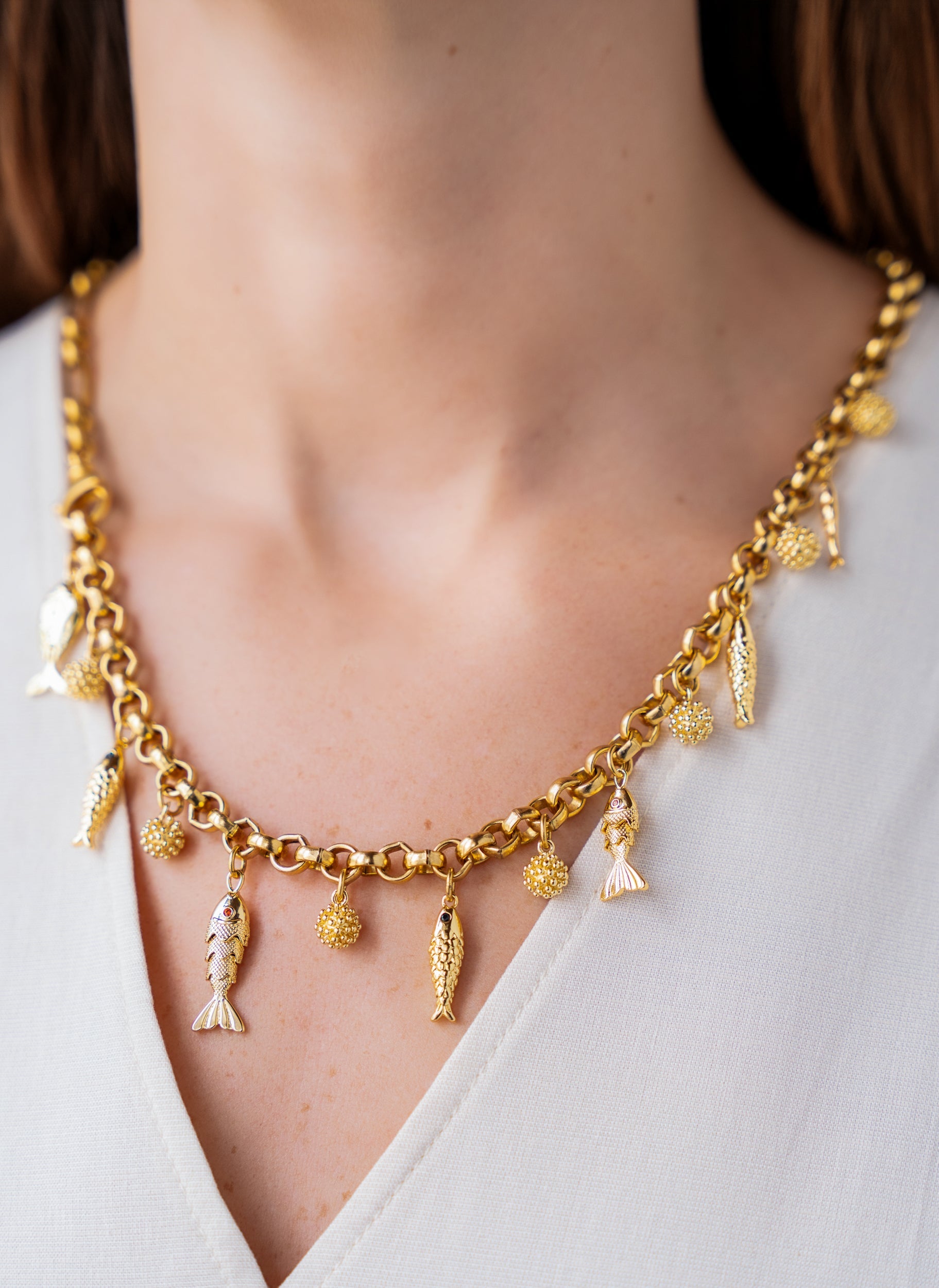 Convertible gold fish charm necklace with dangling fish and textured bead charms worn as both a lariat and classic chain necklace.