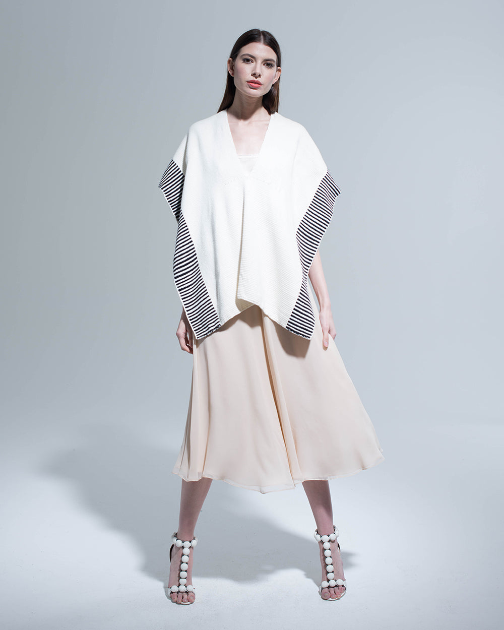 Model wearing Striped Edge Cotton Manta in cream and gray, standing on a light background